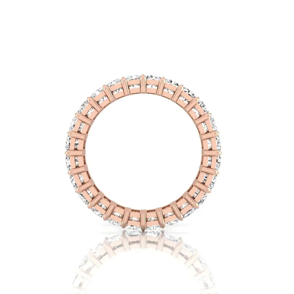 A close-up of the Full Diamond Eternity Ring showcases its thin 18KT rose gold band adorned with a continuous row of small, sparkling F color diamonds with VS clarity, reflecting upright on a white surface.