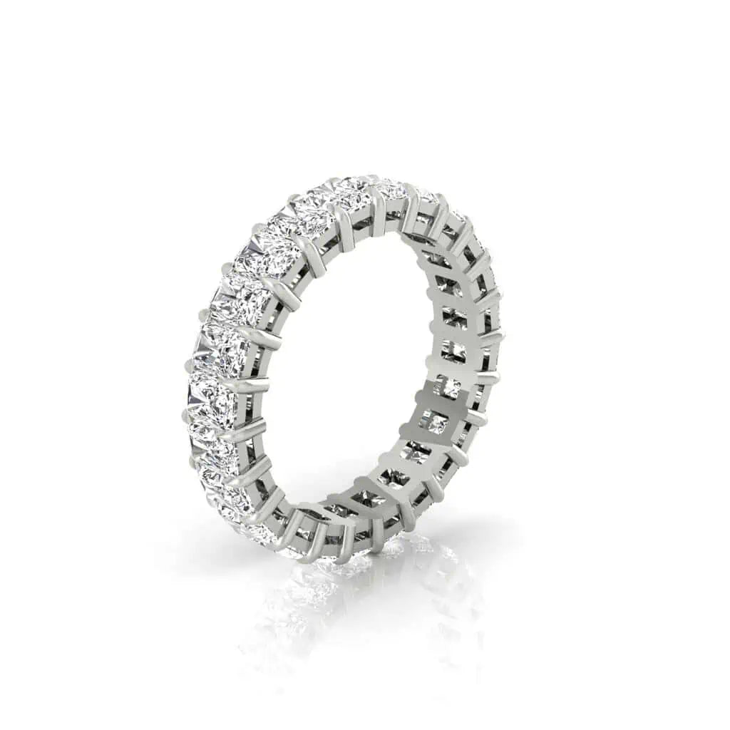 The Full Diamond Eternity Ring is crafted in 18KT gold and adorned with a continuous band of round clear gemstones, likely diamonds, featuring F color and VS clarity. It exudes a luxurious sparkle against its reflective white background.