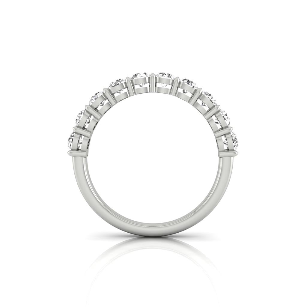 The Half Diamond Eternity Ring, set with sparkling gemstones on its top half, beautifully mimics F Color VS Clarity diamonds. Displayed upright on a reflective white surface, it radiates elegance.