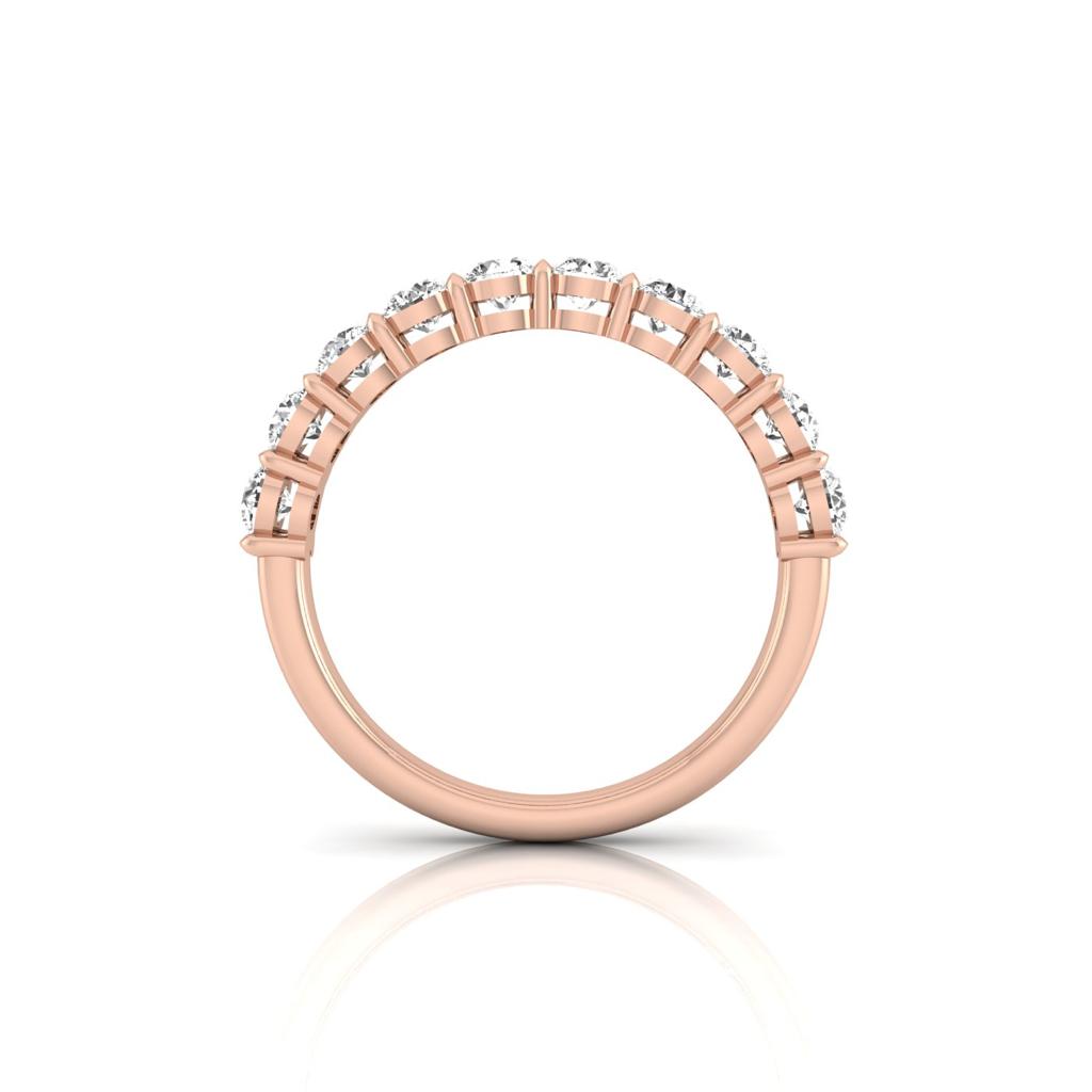 The Half Diamond Eternity Ring, made from 18KT rose gold and featuring small round diamonds set along the top half of the band, is shown from a side angle on a reflective white surface.