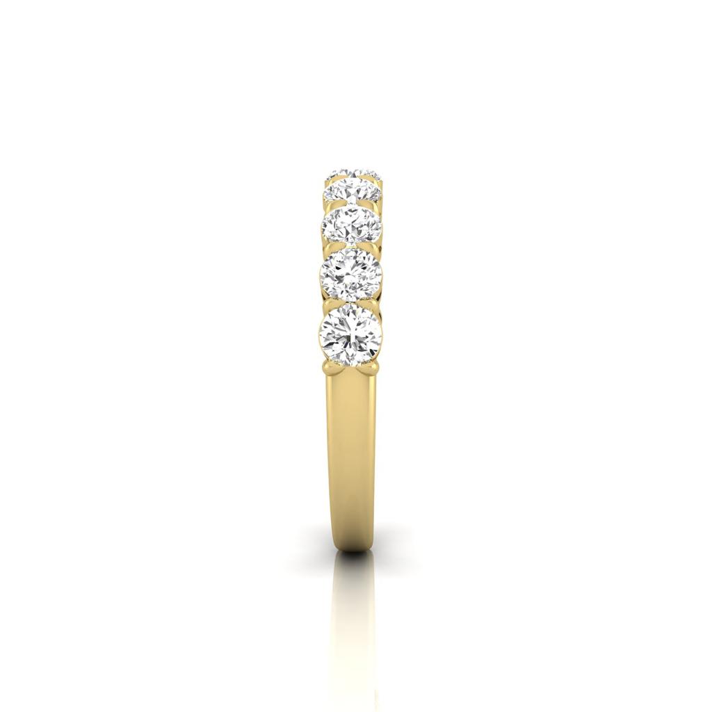 The Half Diamond Eternity Ring, crafted from 18KT gold, features a row of seven sparkling diamonds. The band stands upright against a plain white background, highlighting its elegance and simplicity.