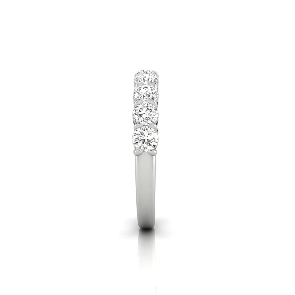 The Half Diamond Eternity Ring, adorned with six sparkling round diamonds in custom carat weights set in a straight line, is elegantly displayed on a plain white background, highlighting its timeless beauty.
