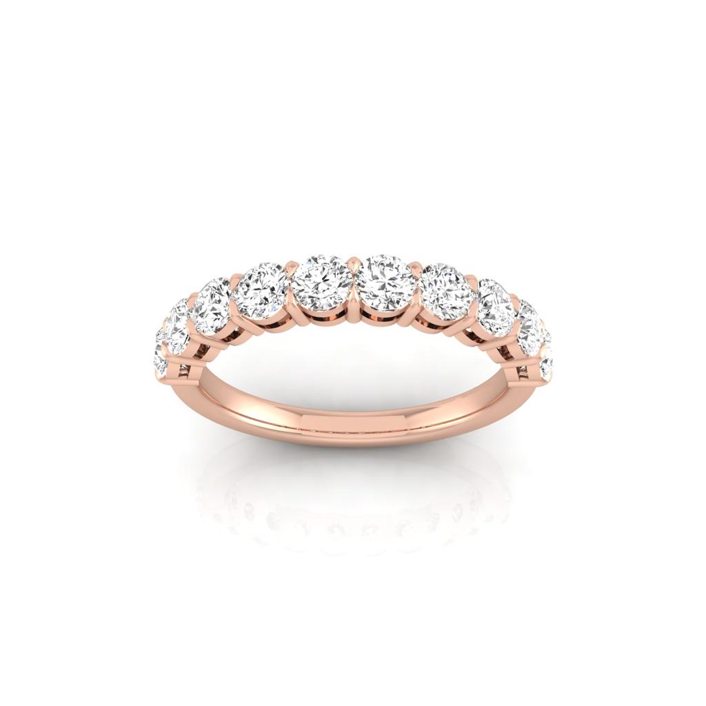 The Half Diamond Eternity Ring is an 18KT rose gold piece featuring a row of sparkling round diamonds along the band, showcased upright on a reflective surface to highlight its elegant design crafted with custom carat weights.