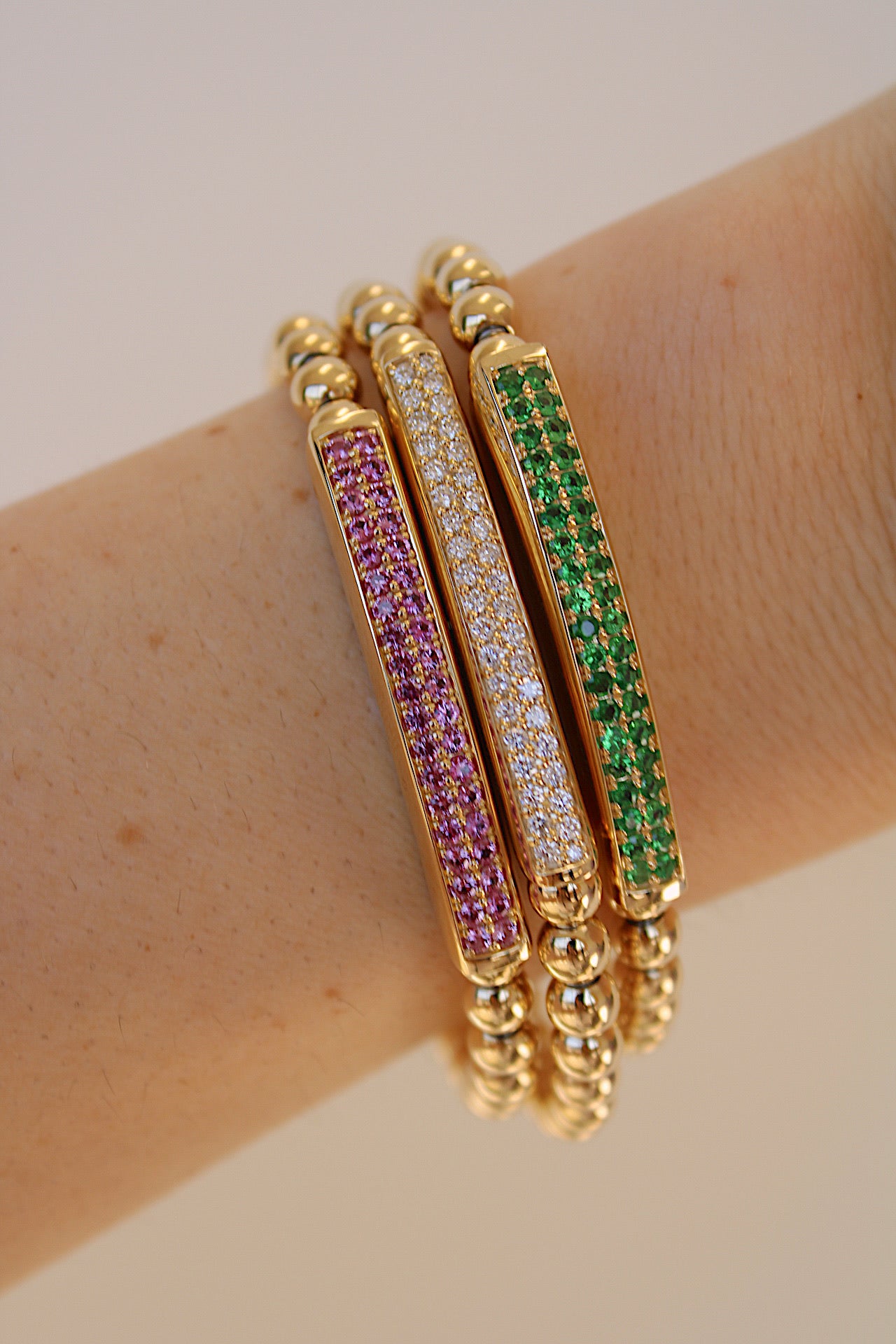 The Pink Sapphire Lennon Stretchy Bracelet from Janet Heller Fine Jewelry adorns a lightly freckled arm. It features rectangular inlays with purple, clear, and green gemstones for an elegant yet vibrant look.