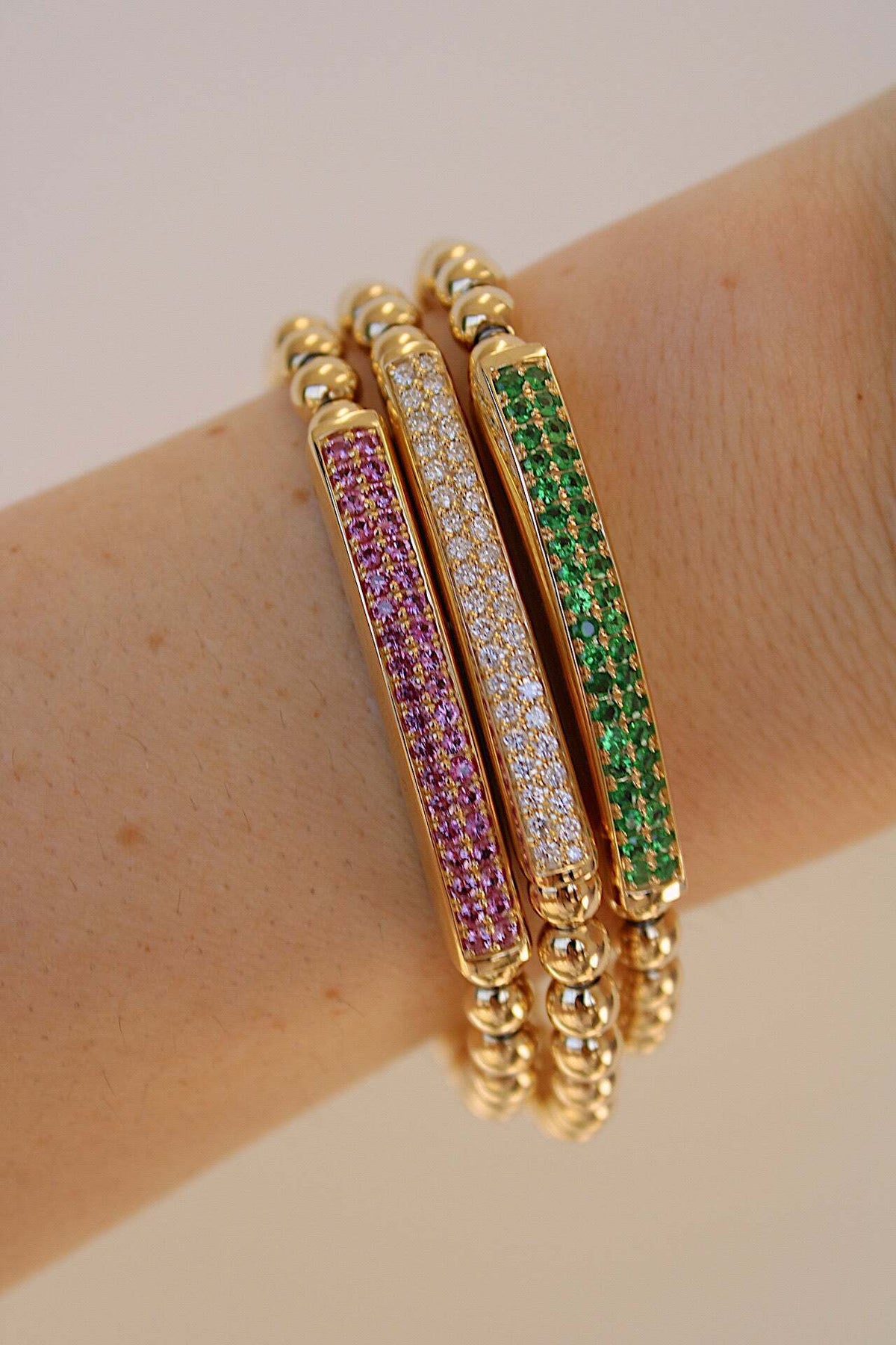 The Pink Sapphire Lennon Stretchy Bracelet from Janet Heller Fine Jewelry adorns a lightly freckled arm. It features rectangular inlays with purple, clear, and green gemstones for an elegant yet vibrant look.