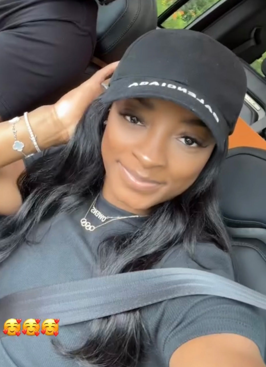 A woman with long black hair, wearing a black cap and t-shirt, smiles in the car while showing off two Diamond Rings Necklaces. She sports bracelets on her wrist and adds excitement for a final sale with smiling face emojis.