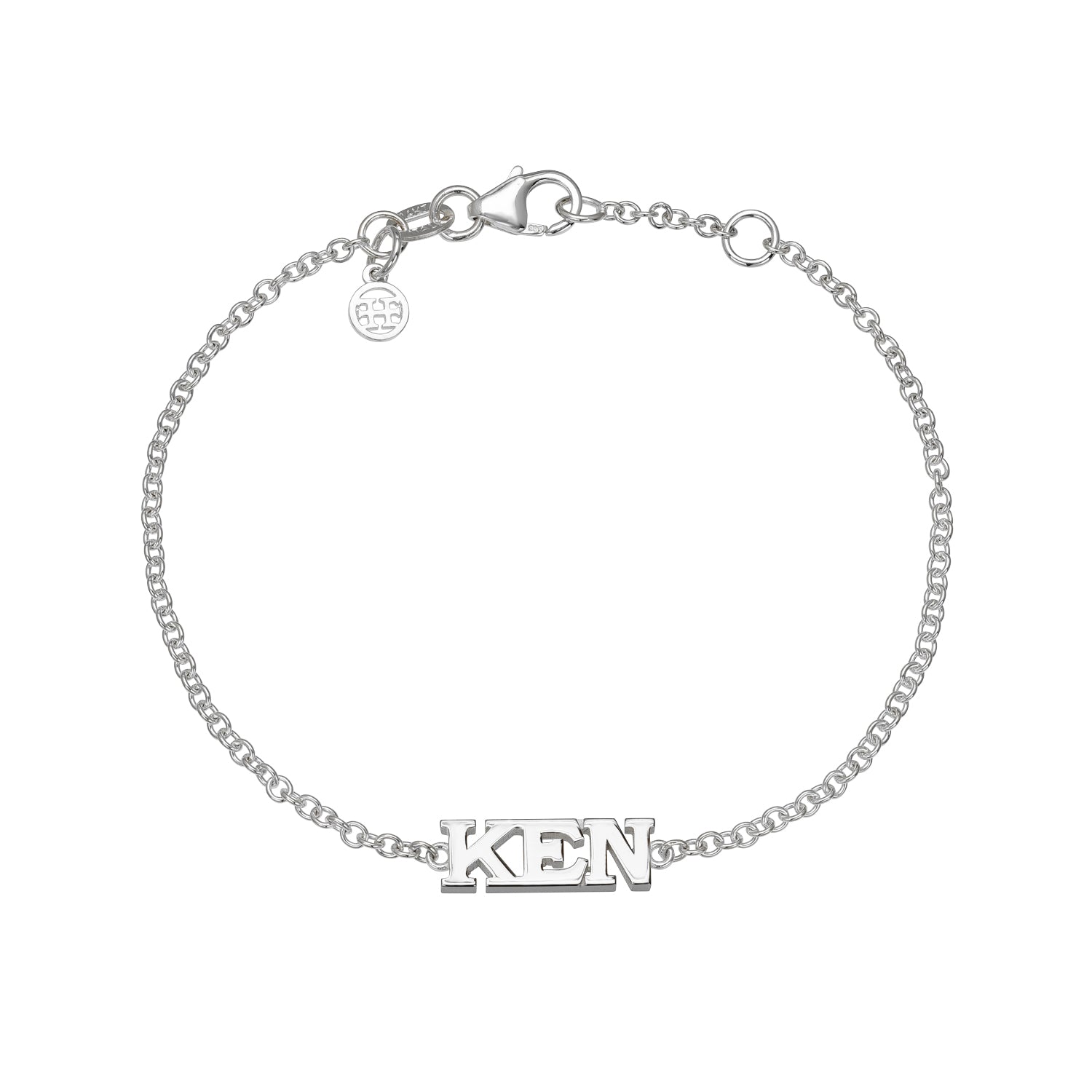 The Block Name Bracelet is a silver chain featuring KEN as a central charm and includes a small round tag with engraved initials near the clasp.