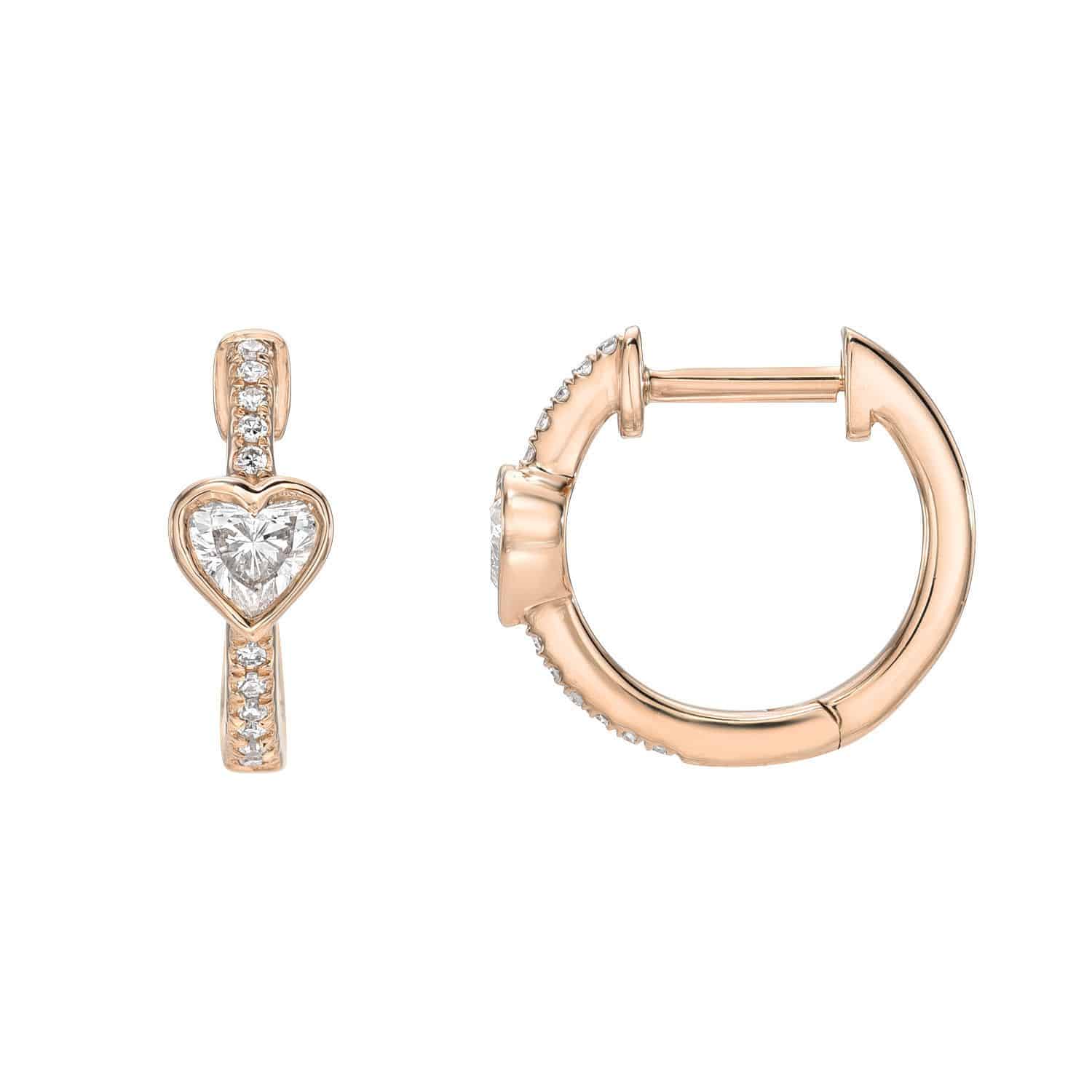 Diamond Amore Huggies by Janet Heller: gold hoop earrings with a heart-shaped clear gemstone and small round gemstones on the front. One earring is displayed from the front, the other from the side.
