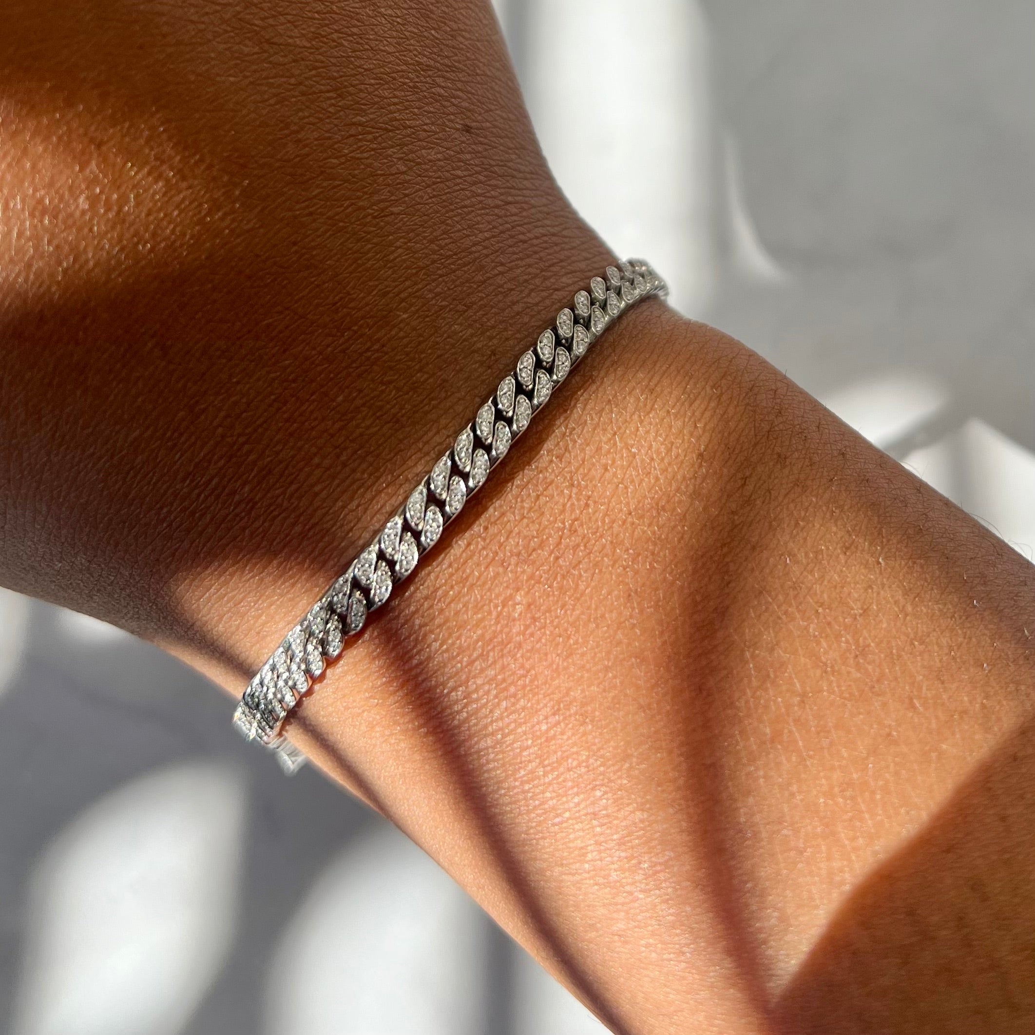 A close-up of a persons wrist adorned with the Diamond Cuban Link Hattie Bracelet by Janet Heller Fine Jewelry; its twisted design shimmers in the light. The softly blurred background enhances the bracelets sparkle and intricate details, showcasing fine craftsmanship.