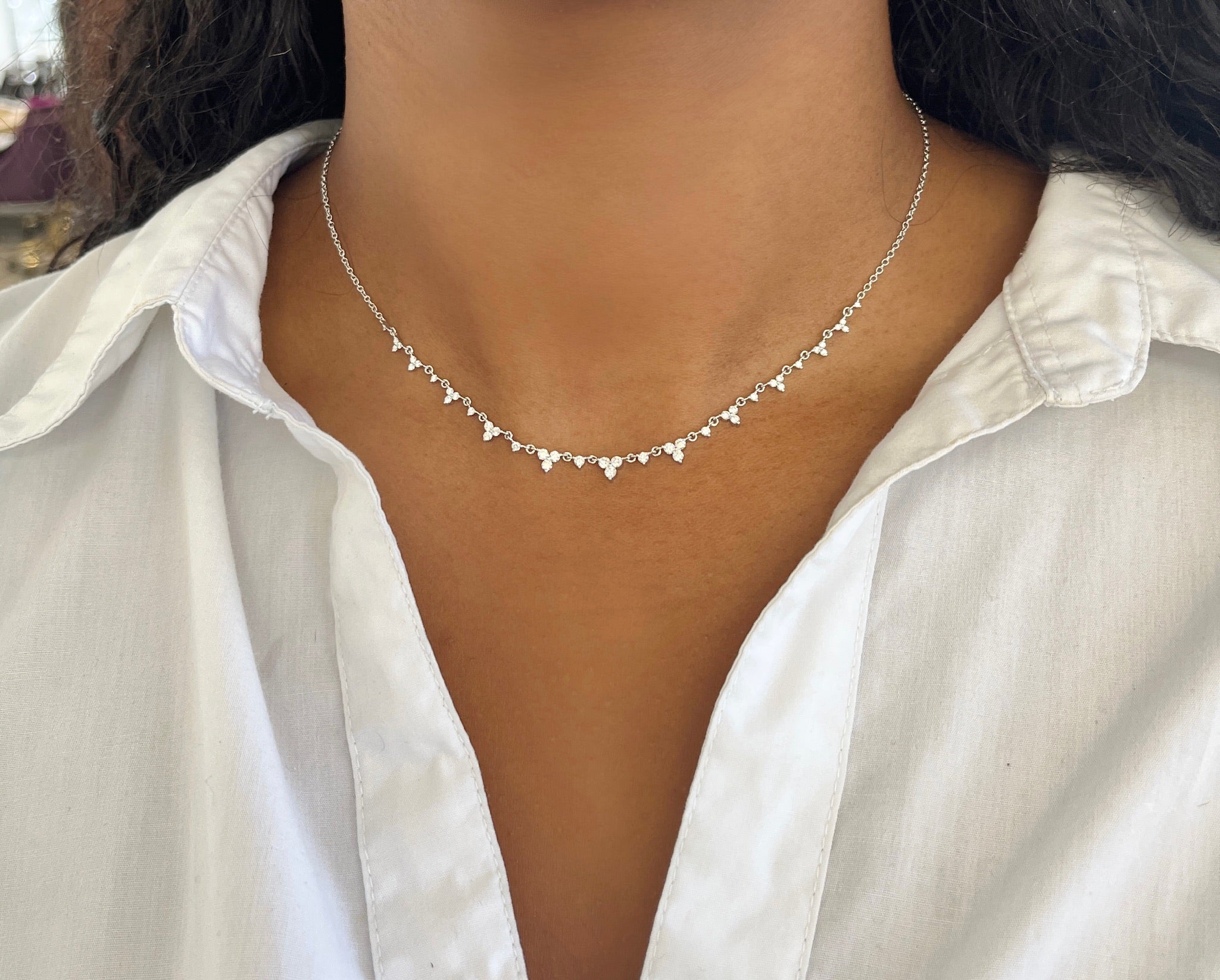 A person wears the Diamond Isabella Necklace by Janet Heller Fine Jewelry, featuring small round pendants. Dressed in a white shirt with only their neck and upper chest visible, the exquisite necklace stands out against the fabric.