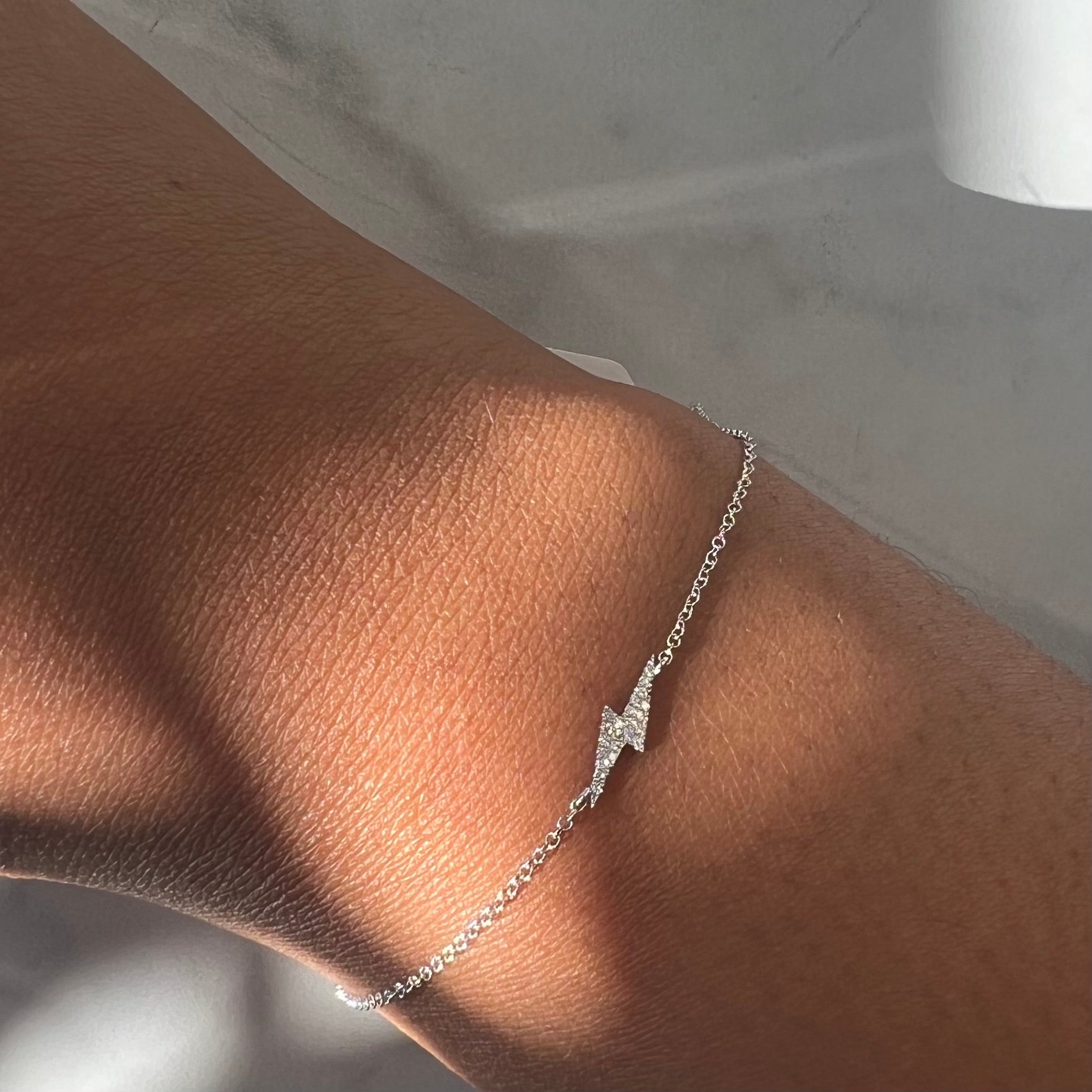 Close-up of a wrist adorned with the Diamond Lightning Bolt Bracelet, a delicate piece that catches light and casts soft shadows on the skin. The out-of-focus background enhances the jewelrys shine.