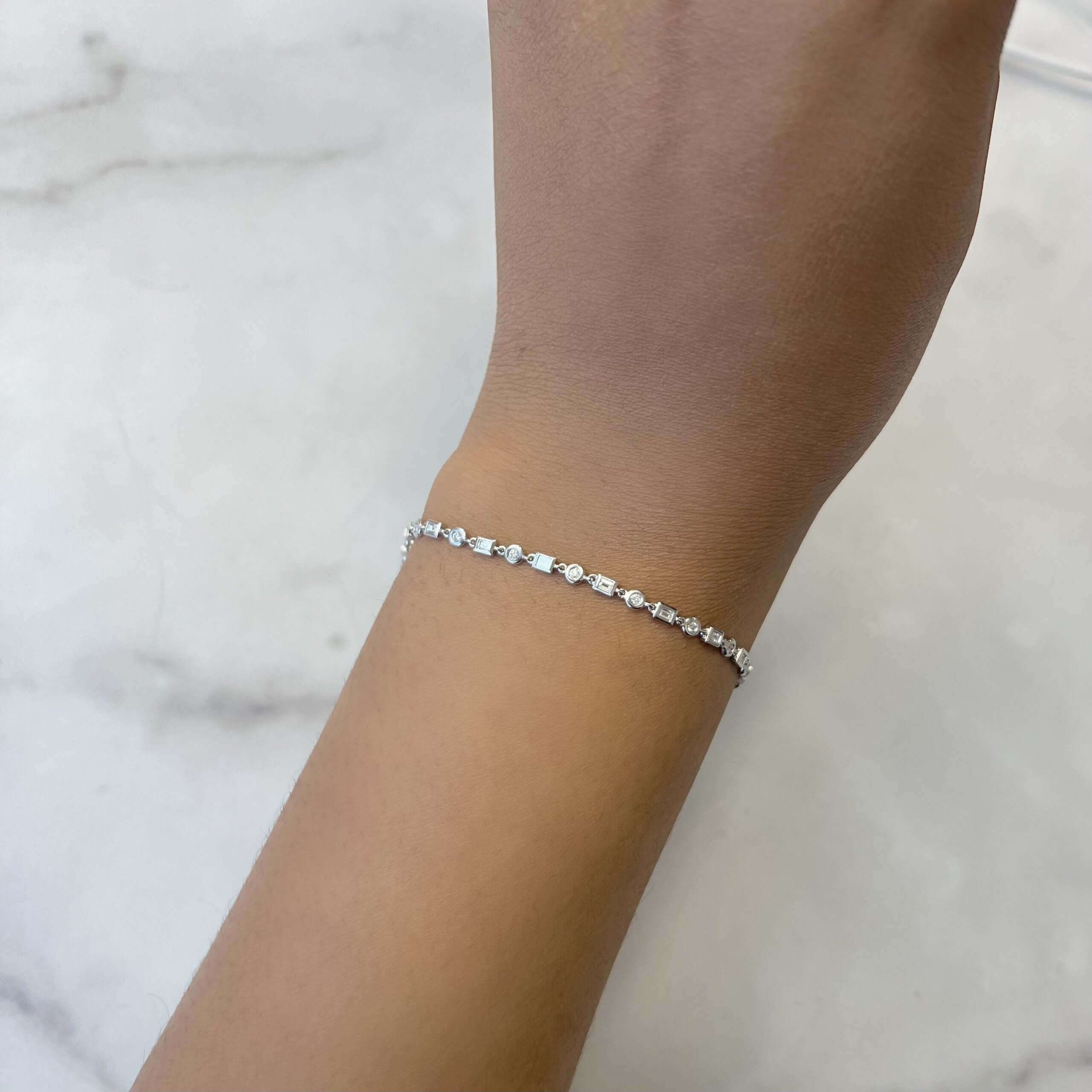 A close-up of a hand wearing the Diamond Nicolette Bracelet, a delicate silver piece adorned with small, evenly spaced clear stones, set against a white marble background and showcasing the elegance and craftsmanship of Janet Heller Fine Jewelry.