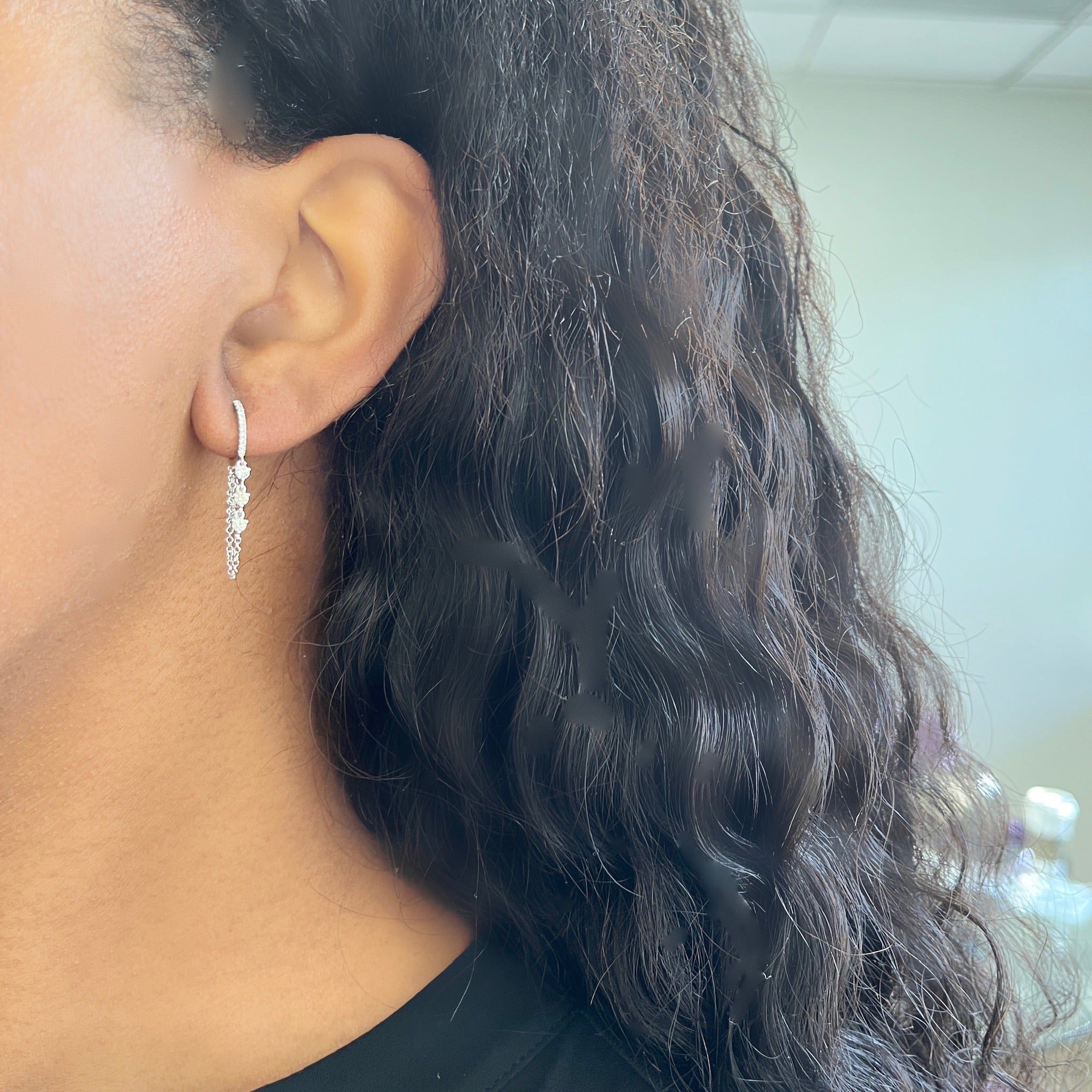 Close-up of a person with long, wavy black hair wearing Layered Diamond Chain Huggies. The silver earrings beautifully reflect the light against a softly blurred background.