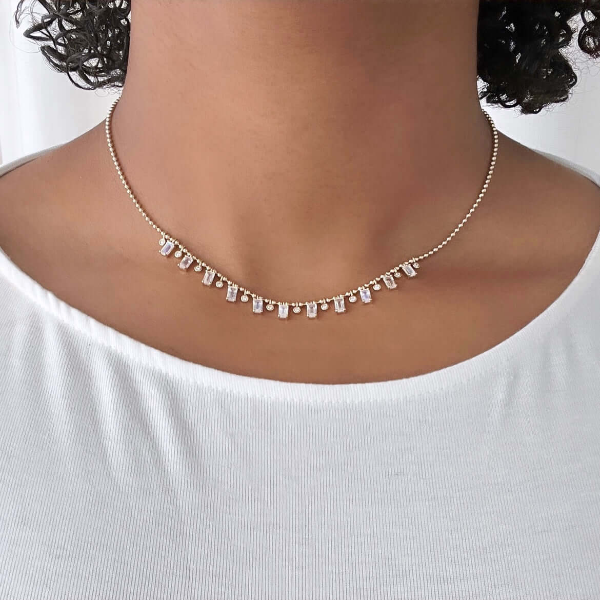 The Beaded Bezel & Moonstone Diamond Necklace from Janet Heller Fine Jewelry is crafted in 14KT gold. It features emerald-cut moonstone pendants and round dangling diamonds. The necklace can be worn on its own or layered with other chains.