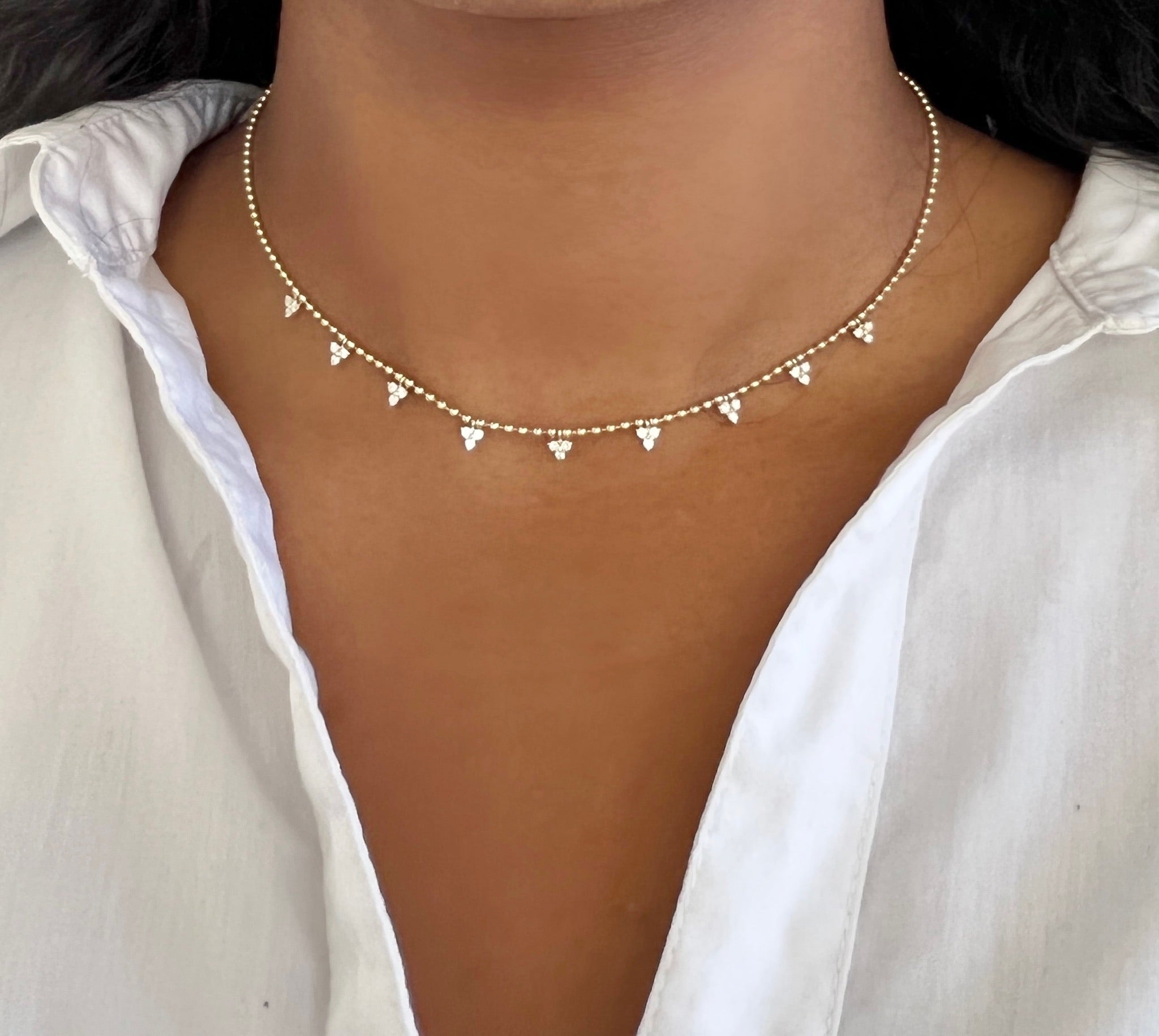 A person in a white open-collar shirt wears the Beaded Diamond Cluster Necklace from Janet Heller Fine Jewelry, featuring grape-like pendant clusters adorned with tiny diamonds.