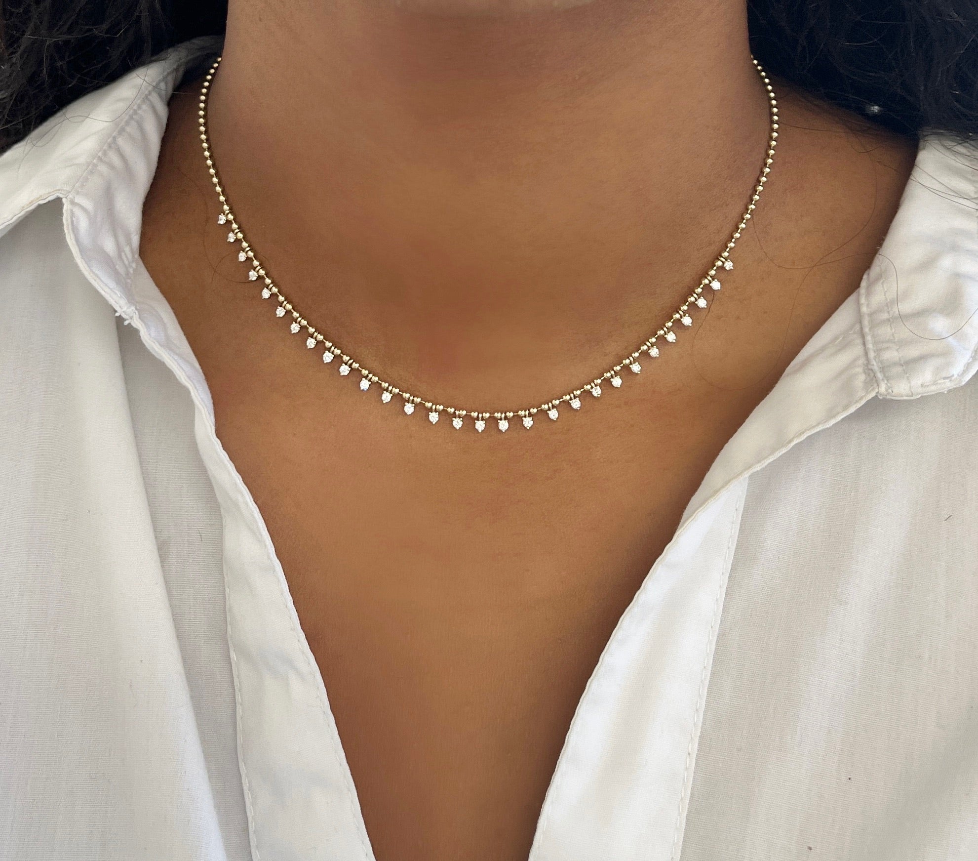 A close-up shows someone in a white shirt wearing the Beaded Diamond Collar Necklace by janethellerfinejewelry, adorned with small hanging pearls. The shirts open collar highlights the elegant jewelry against the skin, set against a blurred background.