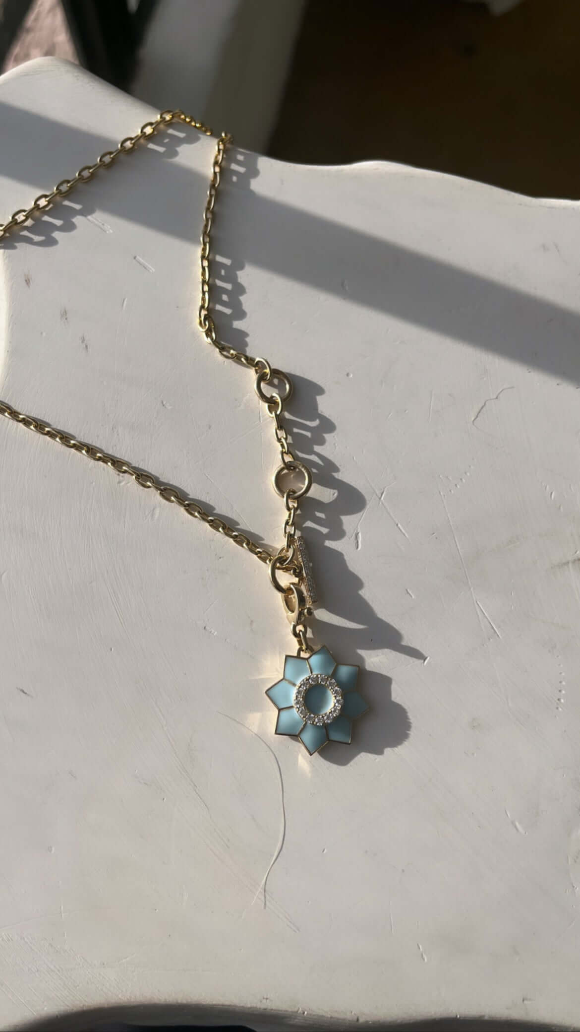 The Enamel & Diamond Flower Charm necklace by Janet Heller Fine Jewelry, features a blue flower pendant with a circular center surrounded by diamonds. The clasp which adorns a single diamond clips easily onto various Janet Heller Fine Jewelry necklaces and chains.