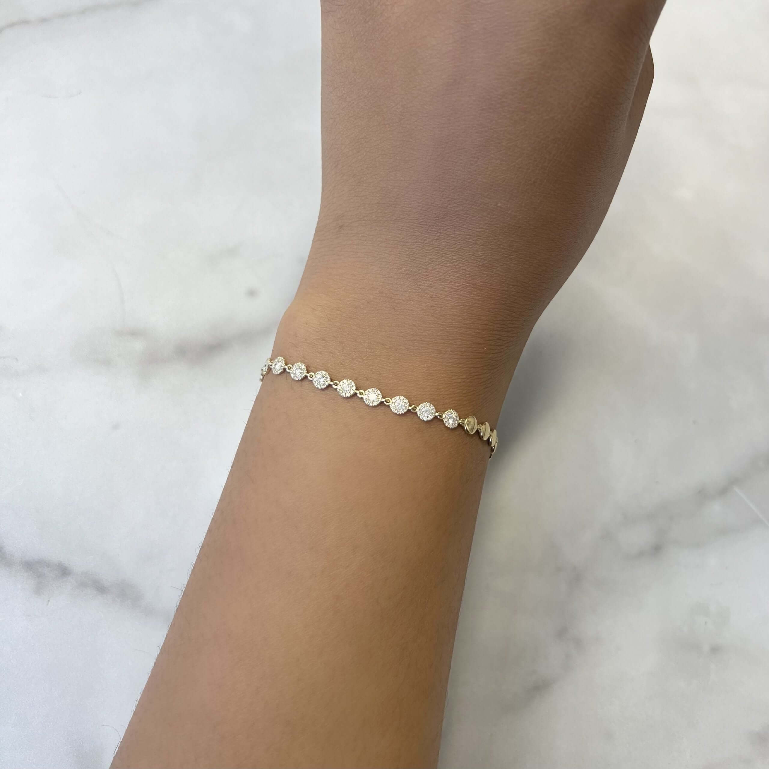 Worn on a wrist against a light marble background, the Diamond Annabel Bracelet from Janet Heller Fine Jewelry features delicate gold with small round charms.