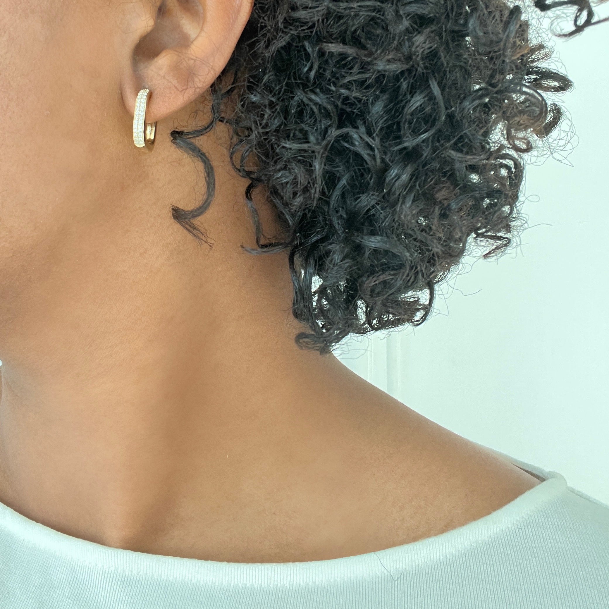Close-up of a person with curly hair wearing Diamond Chunky Square Hoops against a light neutral background.