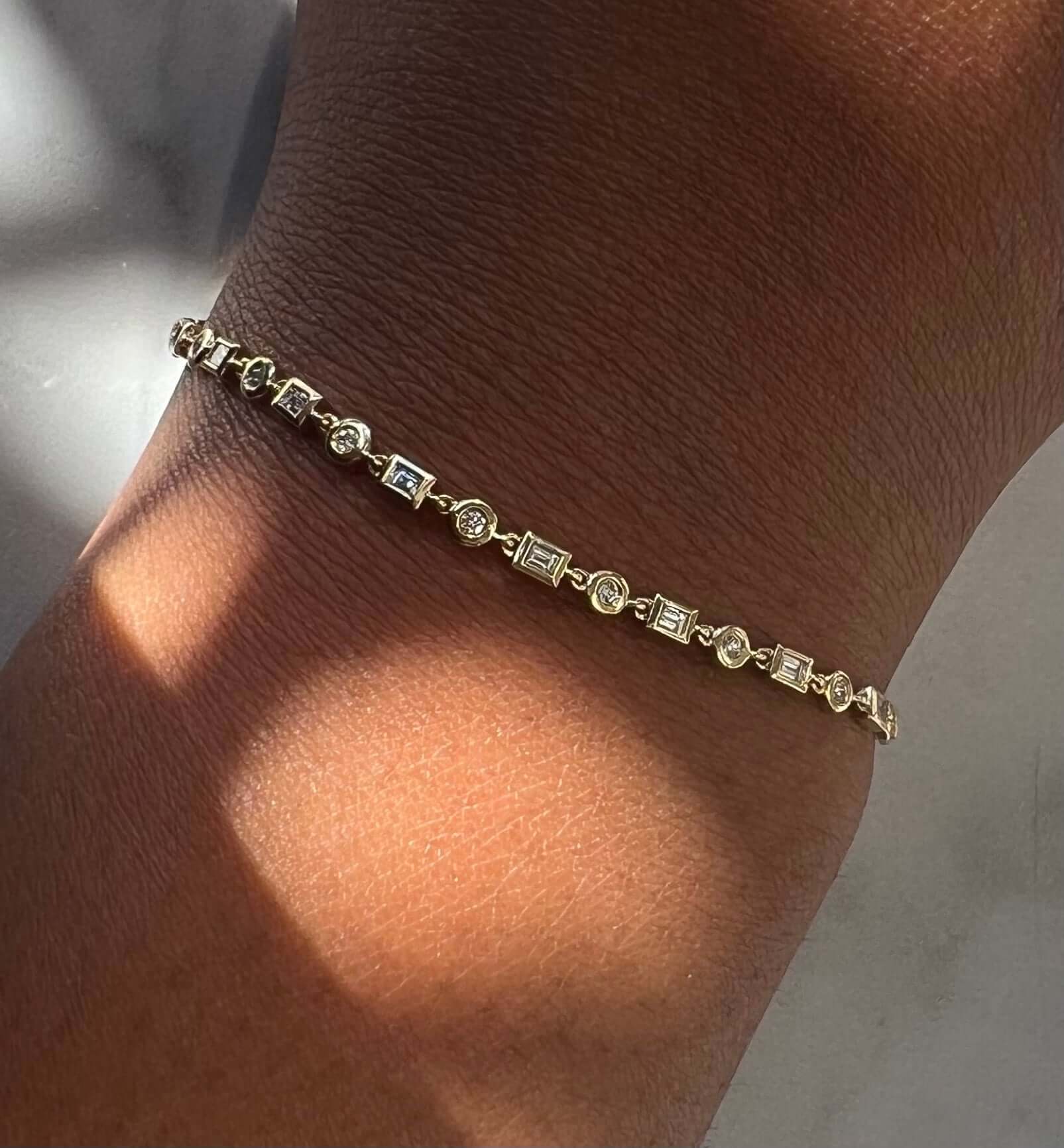 The Diamond Nicolette Bracelet, with its alternating rectangular and round links adorned with small, sparkling stones, graces the wrist. This fine jewelry piece casts a soft shadow in natural light, offering subtle elegance and customizable elements for a personal touch.