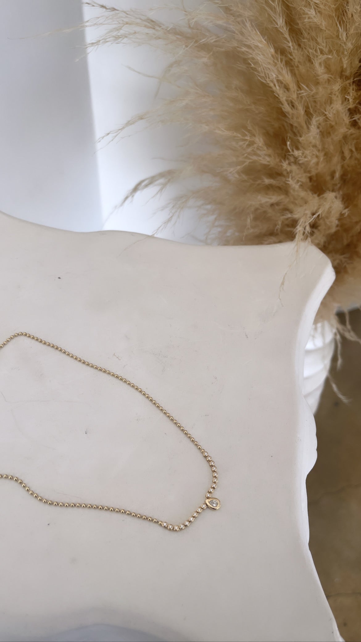 The Diamond Pear Bezel Necklace from Janet Heller Fine Jewelry is crafted in 14KT gold. The delicate gold chain is adorned with round beads and bezel-set round diamonds, finished with a pear-shaped diamond drop in a bezel setting. The necklace can be worn alone or layered with other necklaces.