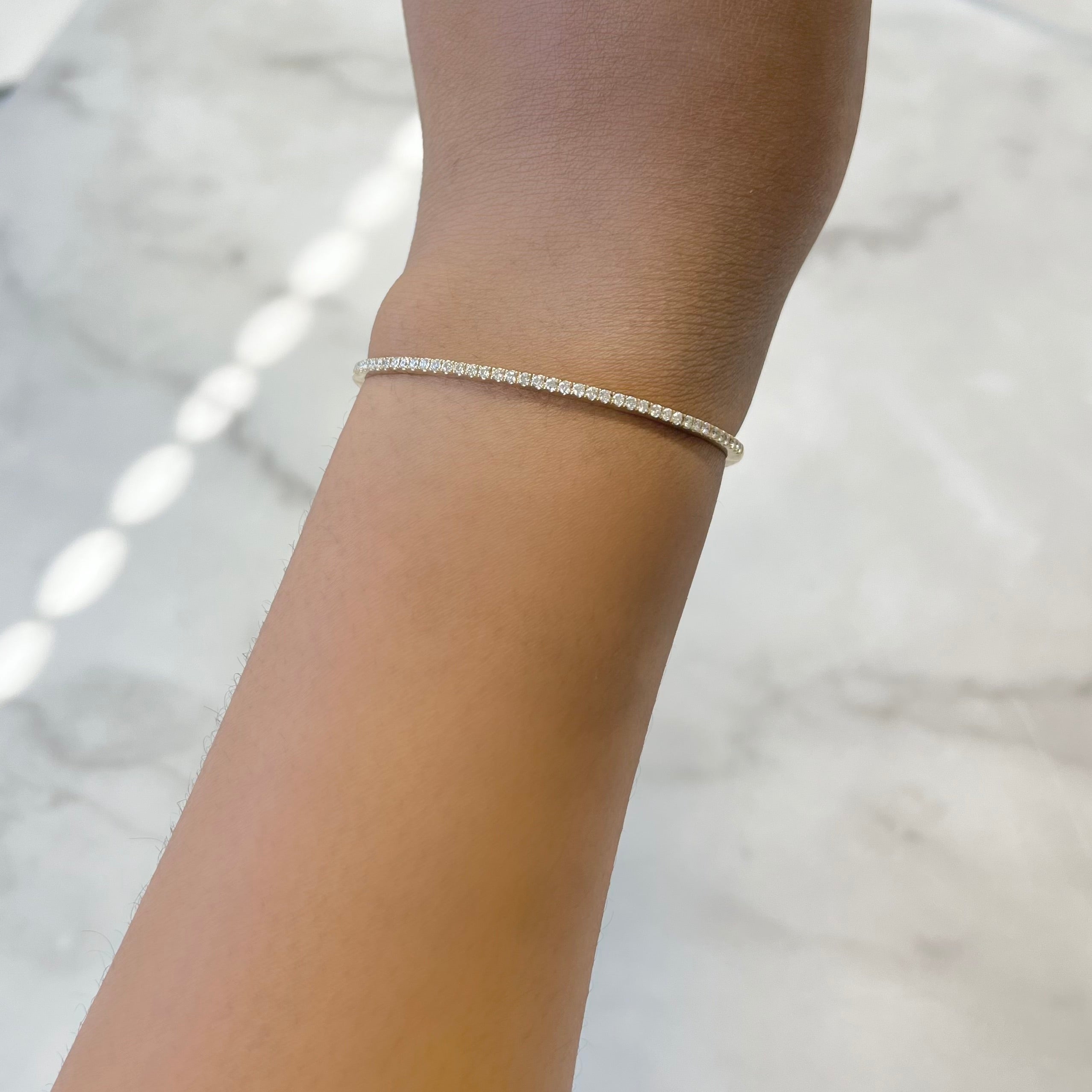 The Diamond Wrenley Bangle graces a light-toned wrist, its subtle sparkle enhancing the smooth, natural backdrop. Bright lighting highlights this elegant design. For customizations or more information, contact inquiries@janethellerfinejewelry.com.