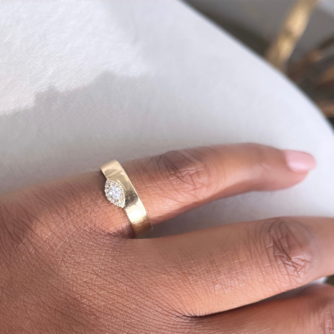 A manicured hand displays the Marquise Diamond Gold Band Ring, a gold band with a leaf-shaped, diamond-encrusted design. The ring rests on a light surface, and the softly blurred background emphasizes its elegance. Available for preorder.