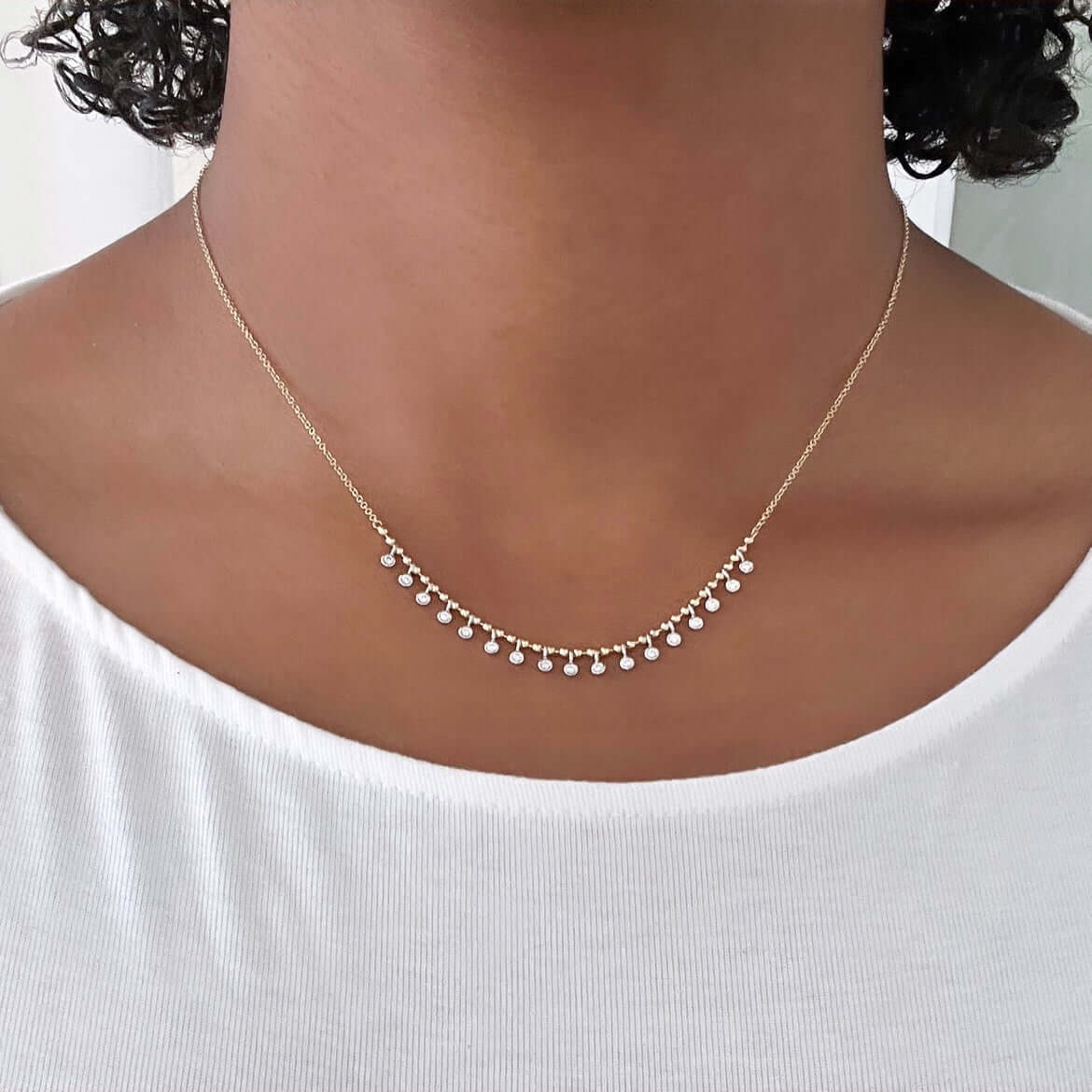 A person wears a Beaded Two Tone Diamond Necklace from Janet Heller Fine Jewelry, with small hanging beads, elegantly resting on their neck and perfectly paired with a white top.