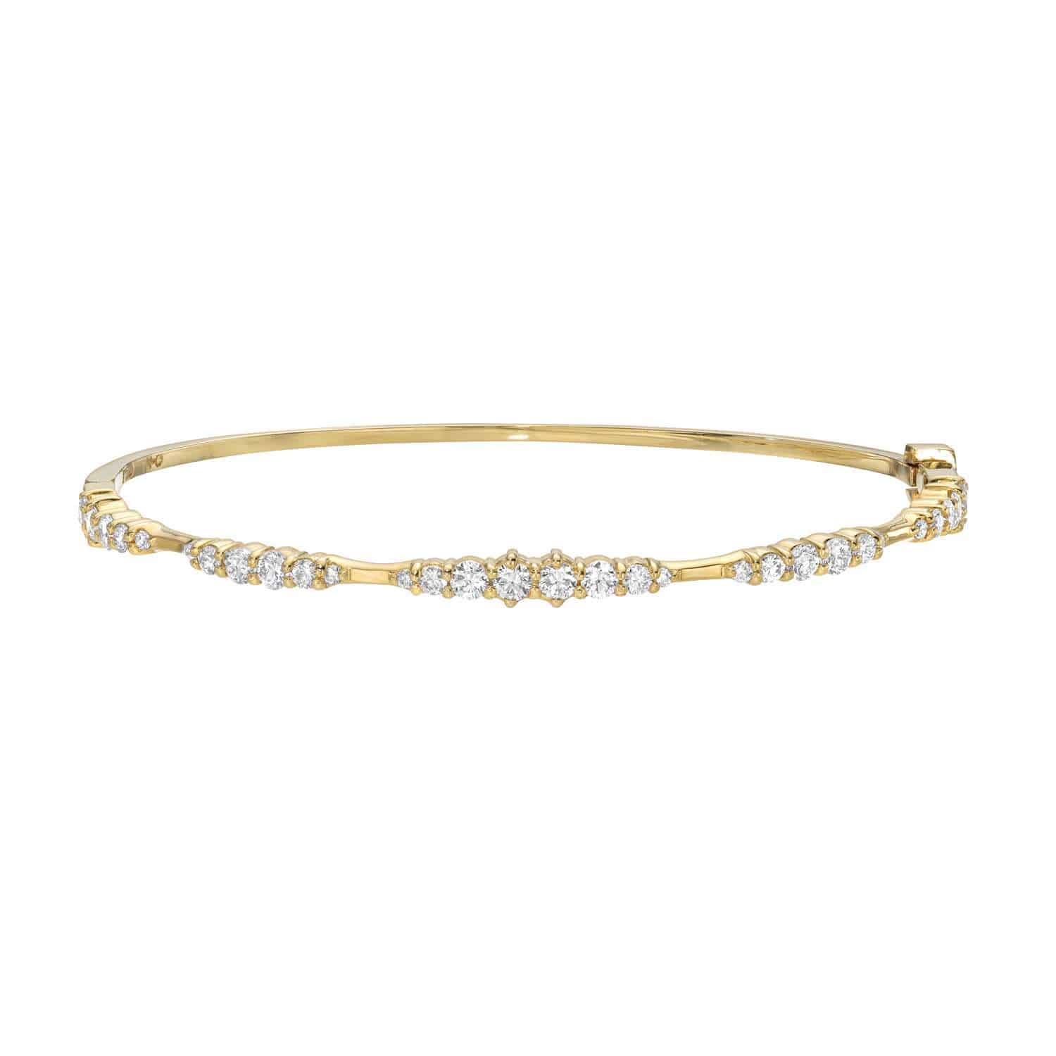 The Graduating Diamond Bangle by Janet Heller Fine Jewelry is a slender gold bracelet adorned with small round diamonds along the top. Its elegant design and latch closure on one side add unparalleled sparkle to any ensemble.