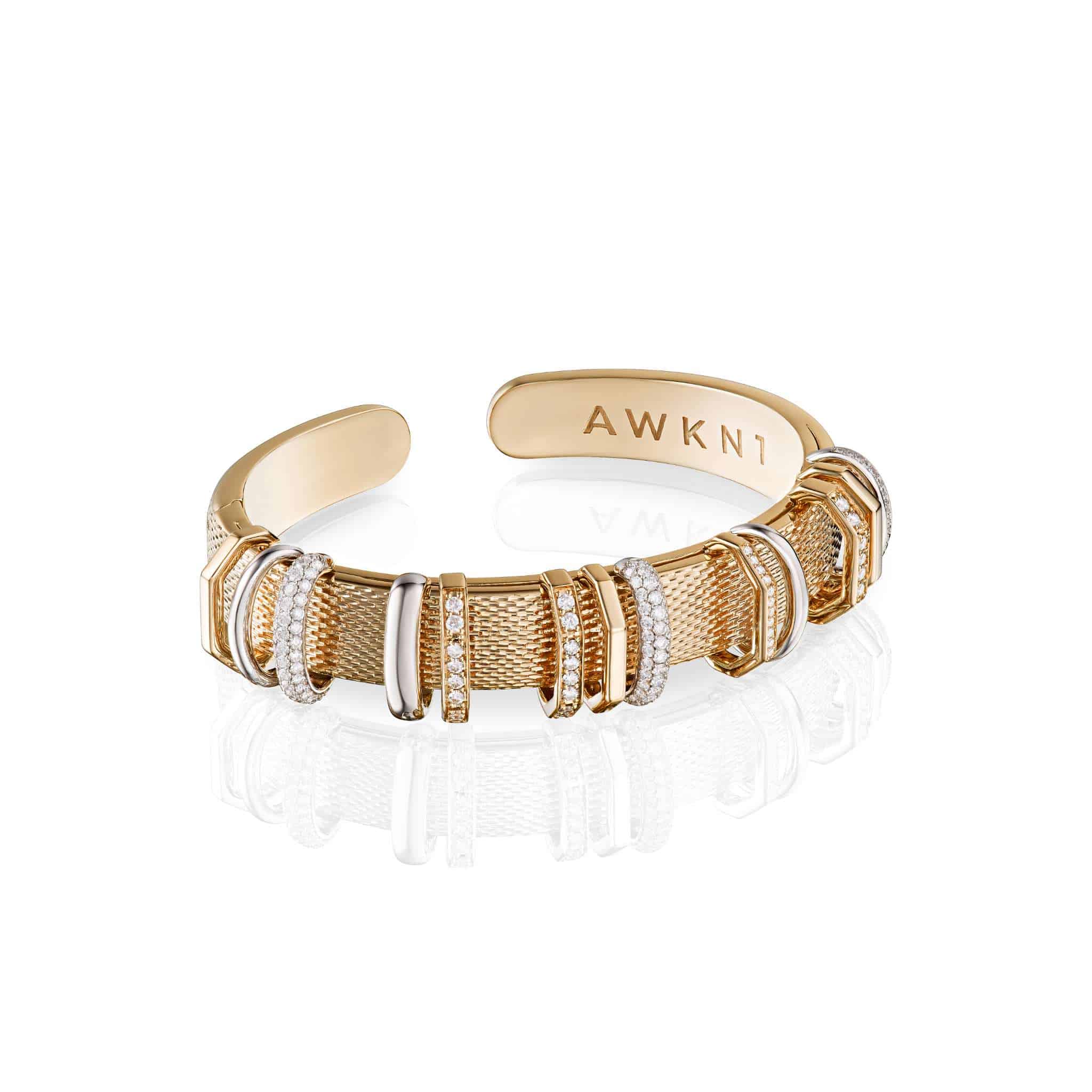 Flinking Whispering Truth Bracelet featuring a gold cuff design with textured and smooth sections, accented by white stones and engraved with AWKN1 on the inner side.