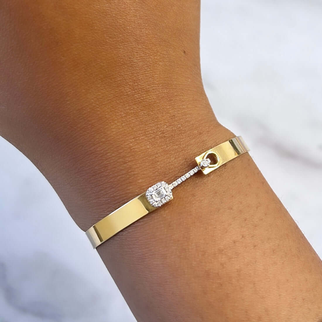 The Diamond Hook Bangle from Janet Heller Fine Jewelry is crafted in 18KT gold and features emerald and round diamonds. The bangle can be worn alone or stacked with other bracelets.