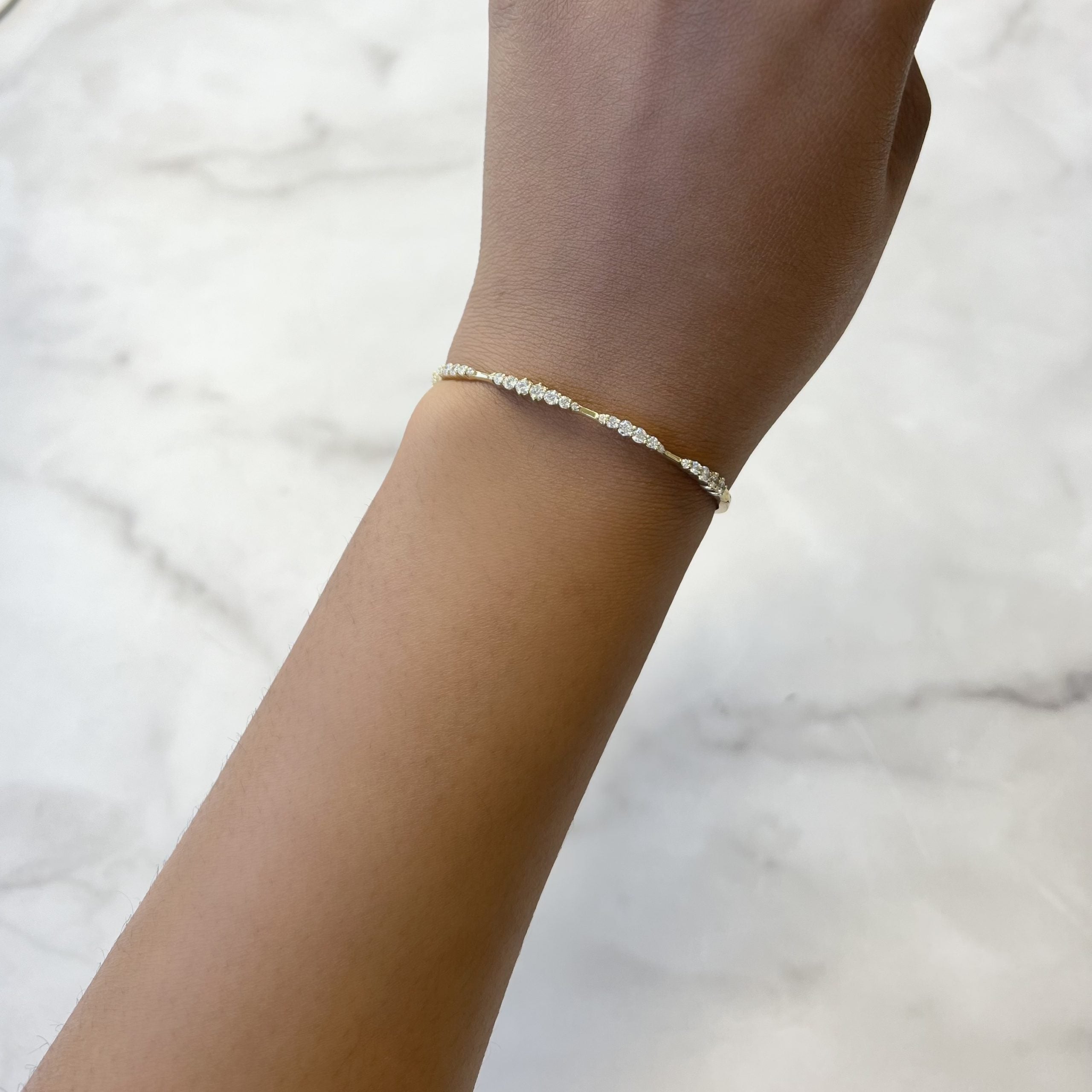 The Graduating Diamond Bangle from Janet Heller Fine Jewelry elegantly adorns a persons wrist against a white marble surface.