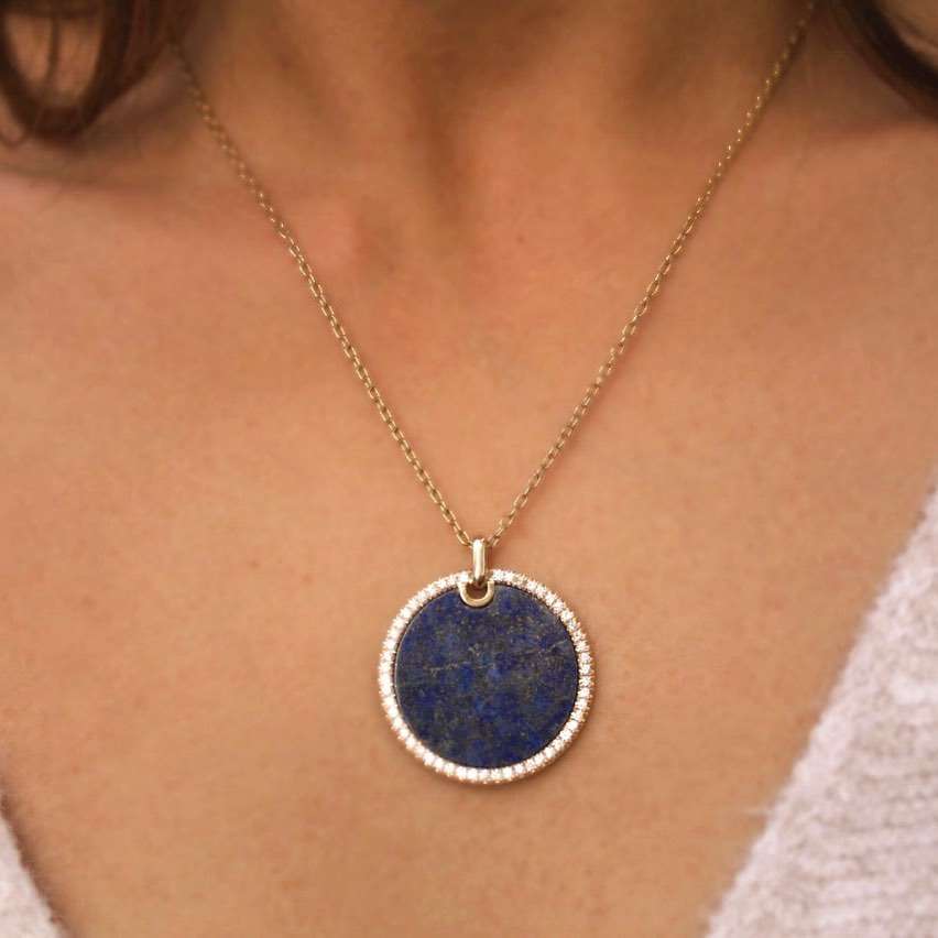 The Large Lapis Pendant Necklace from Janet Heller Fine Jewelry is crafted in 14KT gold. The round lapis charm is edged in diamonds. The necklace can be worn alone or layered with other chains.