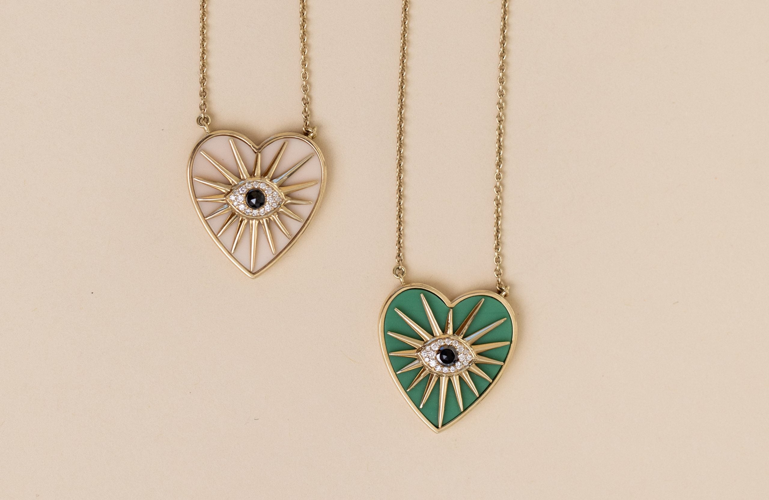 The Green Chrysoprase Heart Burst Necklace from Janet Heller Fine Jewelry features chain links and a gold eye design with radiating lines. The pendant is vibrant green, showcasing a central eye detail against a plain beige background, perfect for highlighting this stunning piece.