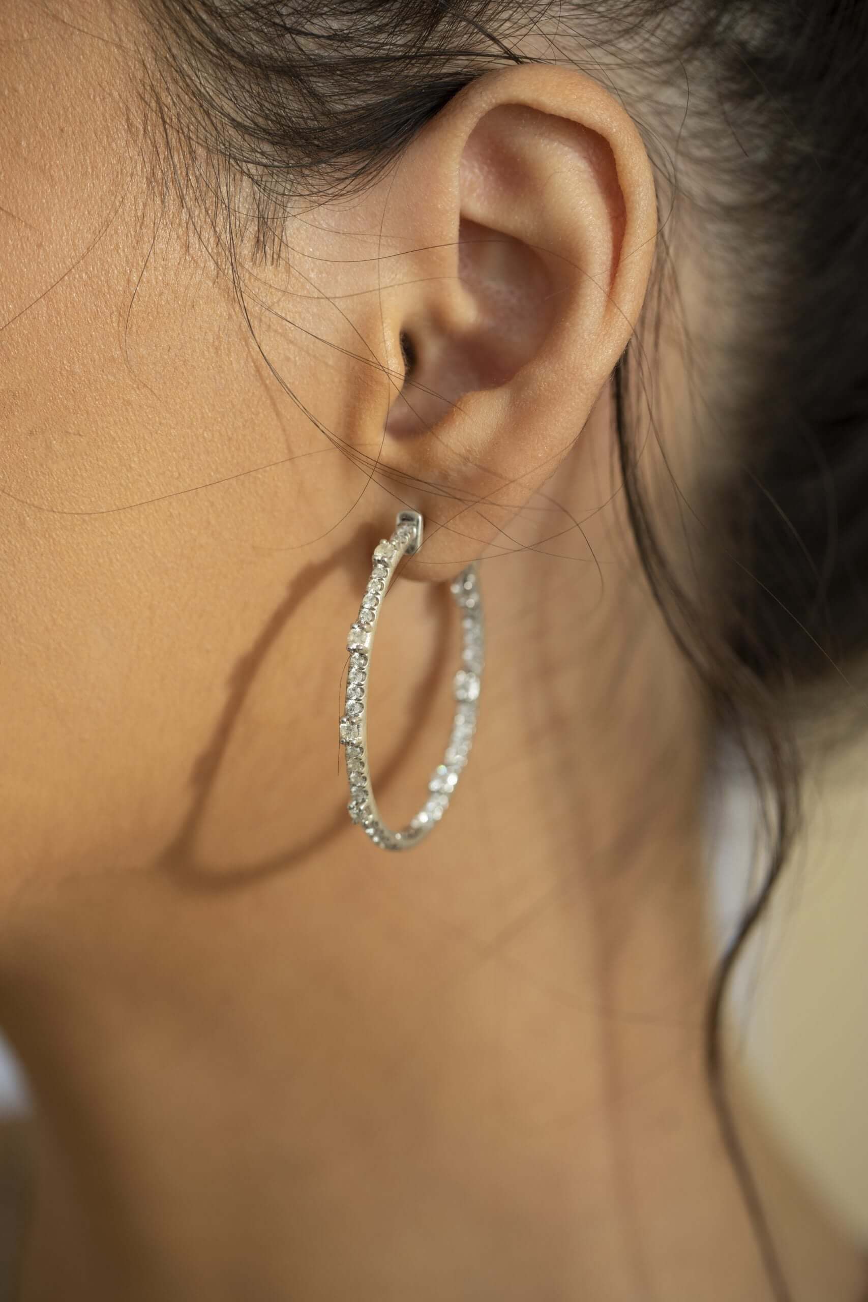 A persons ear is adorned with JanetHellerFineJewelrys Oval Chandler Hoops, a large, textured silver earring that showcases exceptional craftsmanship. The intricately designed hoop stands out as the persons dark hair is tied back, highlighting their smooth skin tone and the earrings elegance.