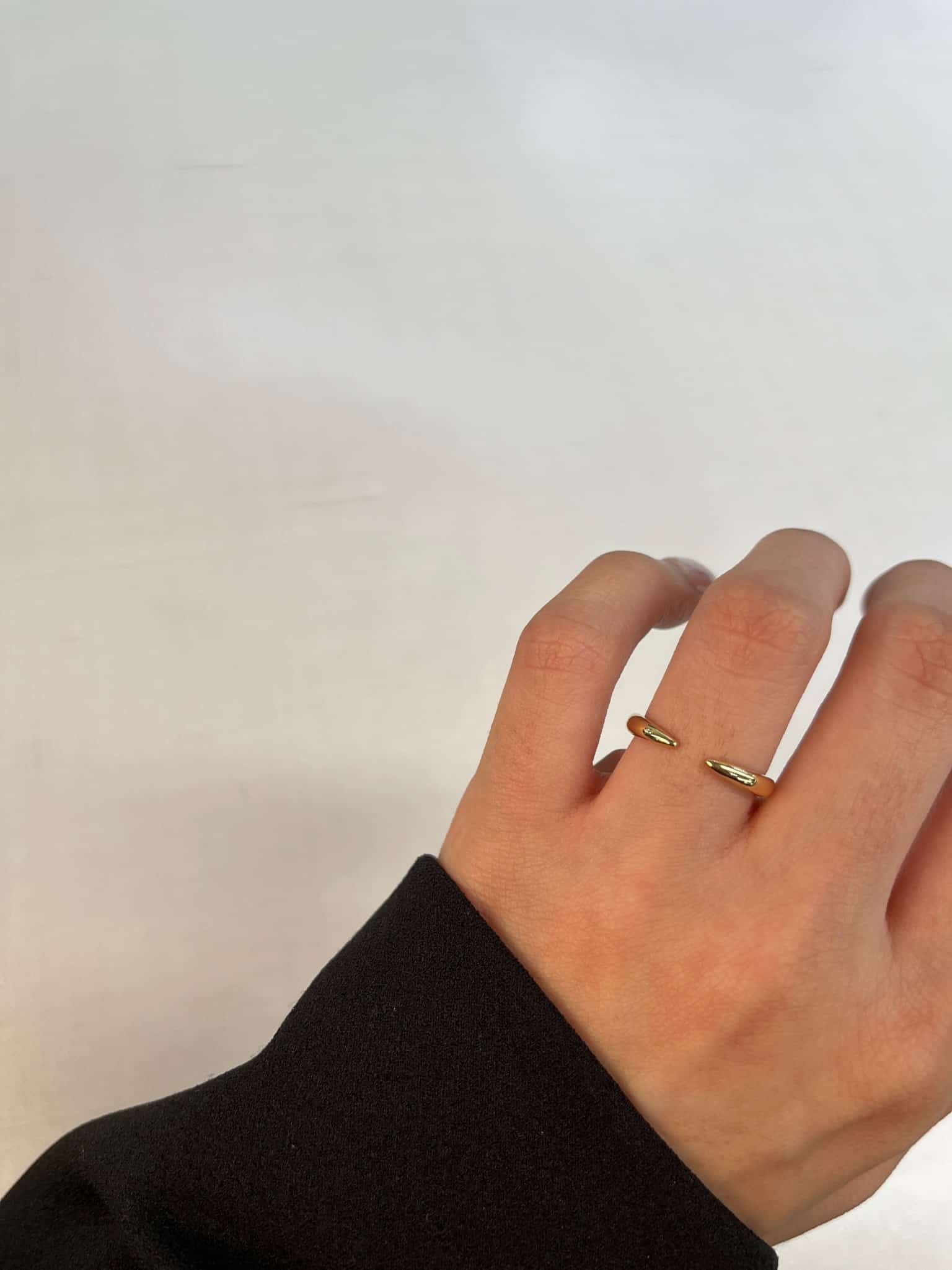 A hand in a dark sleeve is set against a light background, showcasing the Open Plain Gold Cuff Ring by FoundryFineJewelry on the ring finger. This elegant, double-band piece is a statement of understated luxury.