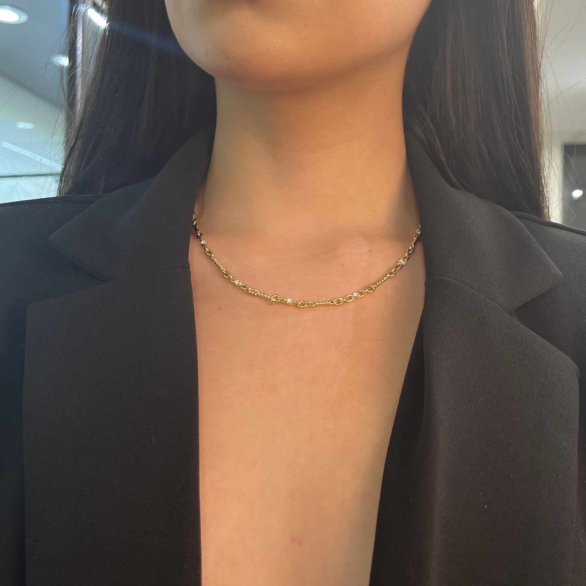 A person in a black blazer with a deep neckline wears the Diamond Belle Necklace from JanetHellerFineJewelry. Their dark hair cascades gracefully, and the well-lit indoor space highlights the necklaces exquisite craftsmanship.