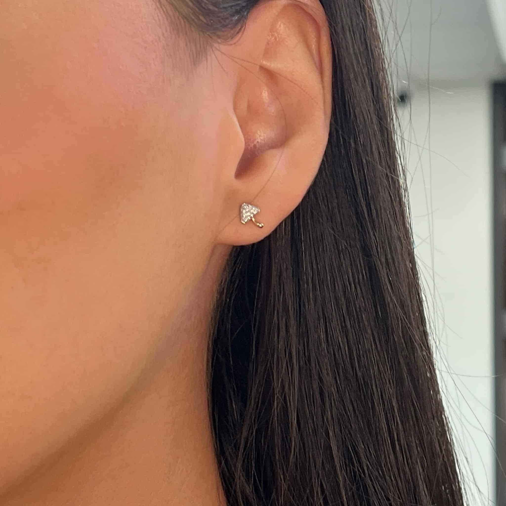 Close-up of an ear wearing a Janet Heller Fine Jewelry Diamond Mushroom Stud, with tiny sparkling crystals. The straight, dark hair frames it perfectly against the artfully blurred background.