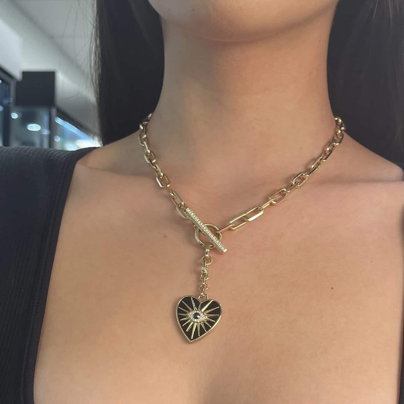 The Black Agate Heart Burst Charm from Janet Heller Fine Jewelry is crafted in 14KT gold. The charm is set in black enamel with gold rays. The center of the pendant features an evil eye with a center black diamond that is surrounded by white diamonds. The diamond clasp clips easily onto various Janet Heller Fine Jewelry chains and necklaces.