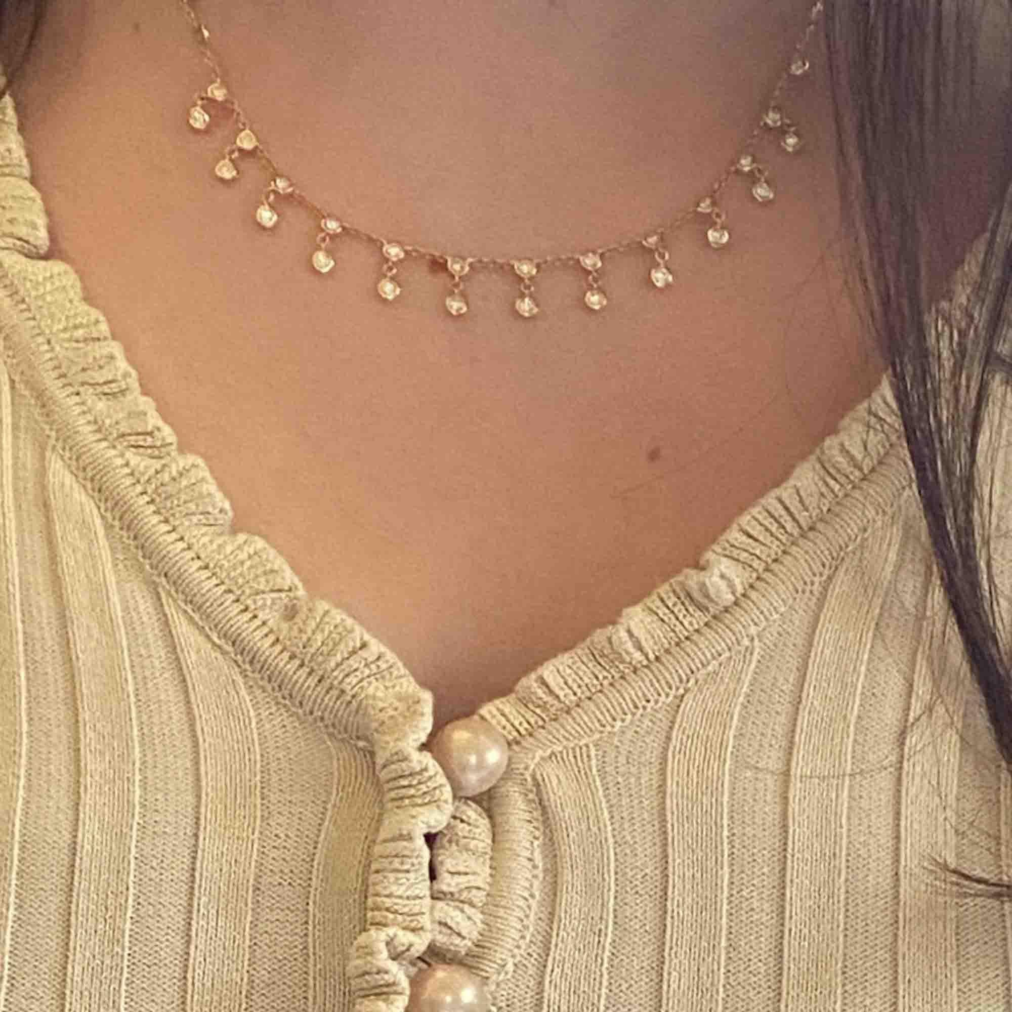 Close-up of a person wearing a cream-colored, ribbed cardigan with pearl buttons and the Double Diamond Bezel Necklace by Janet Heller Fine Jewelry. For jewelry inquiries or custom pieces, please contact us.