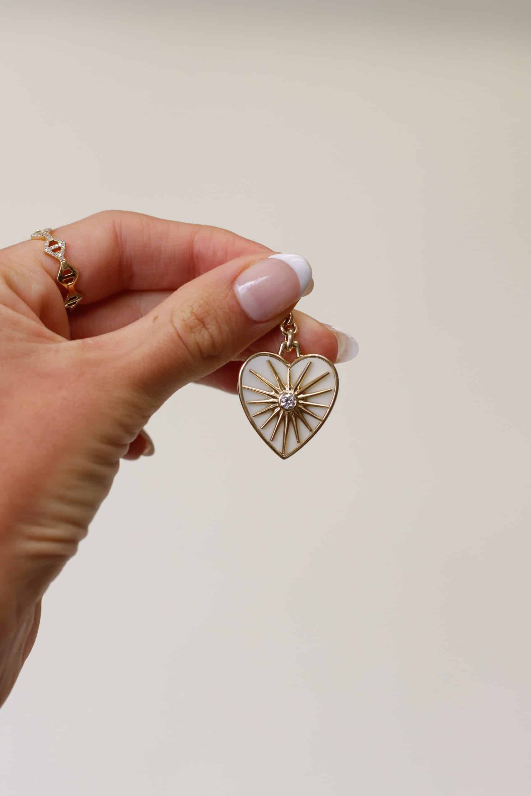 The Cacholong Sun Ray Charm from Janet Heller Fine Jewelry is crafted in 14KT gold. The gold heart-shaped pendant features a starburst design with a central diamond. The diamond clasp clips easily onto various Janet Heller Fine Jewelry necklaces and chains.