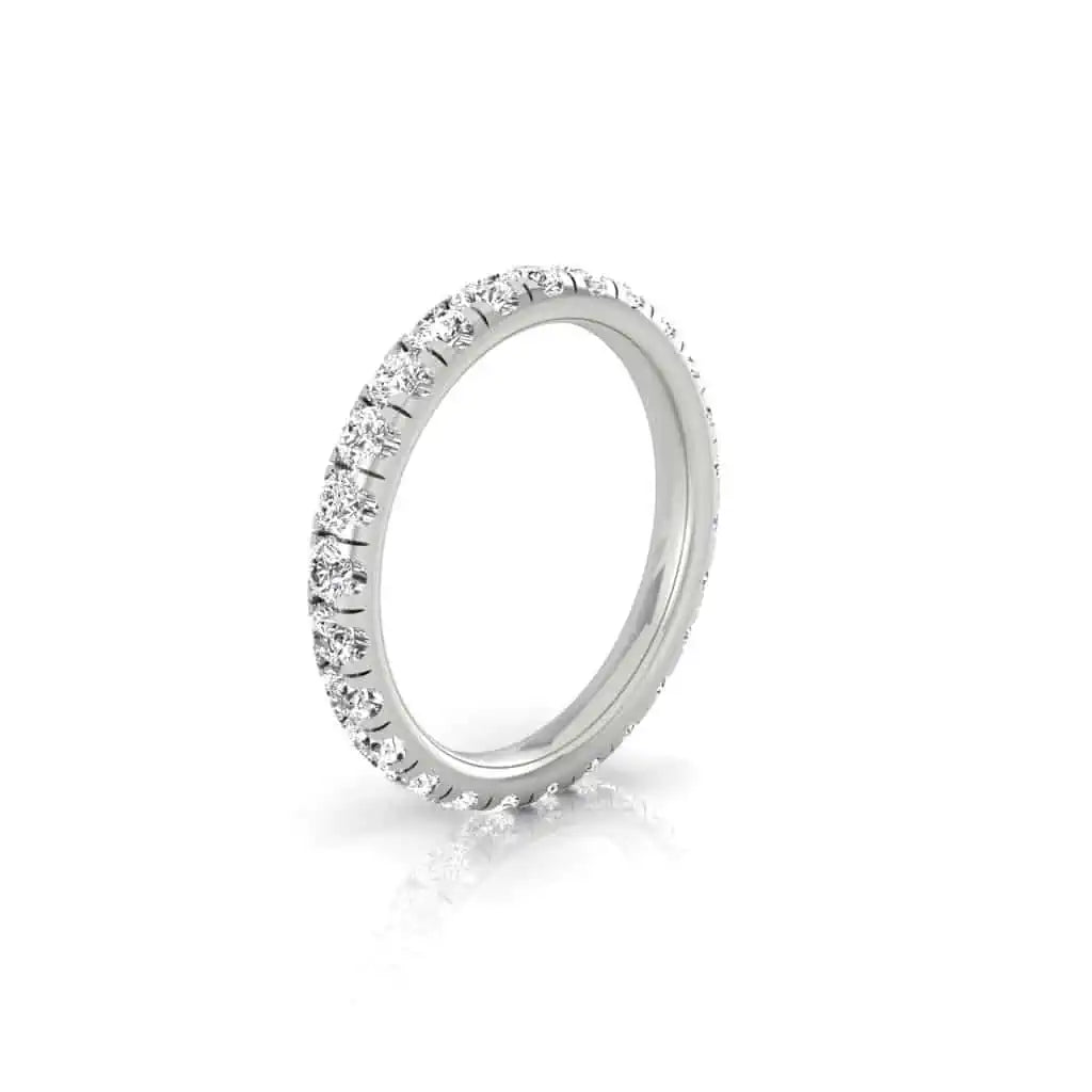 The 1ct Round Diamond Eternity Ring, crafted from silver with small, round-cut diamonds in 18KT gold, displays VS Clarity stones in a captivating continuous sparkle as it stands on a reflective white surface.