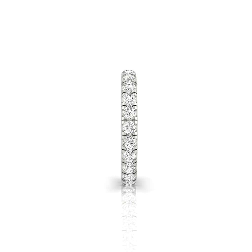 The 1ct Round Diamond Eternity Ring, a thin silver band adorned with small VS clarity diamonds, forms a sparkling continuous circle. Photographed from the side and set against a white background with a gentle reflection, its timeless elegance is undeniable.