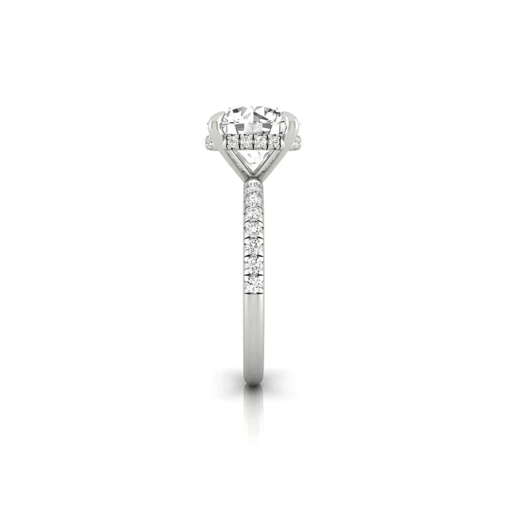 Image of a solitaire engagement ring showcasing a round diamond in a prong setting, with a French Pavé set band, adorned with small diamonds. The design features the Amélie + Hidden Halo for added sparkle against a white background.