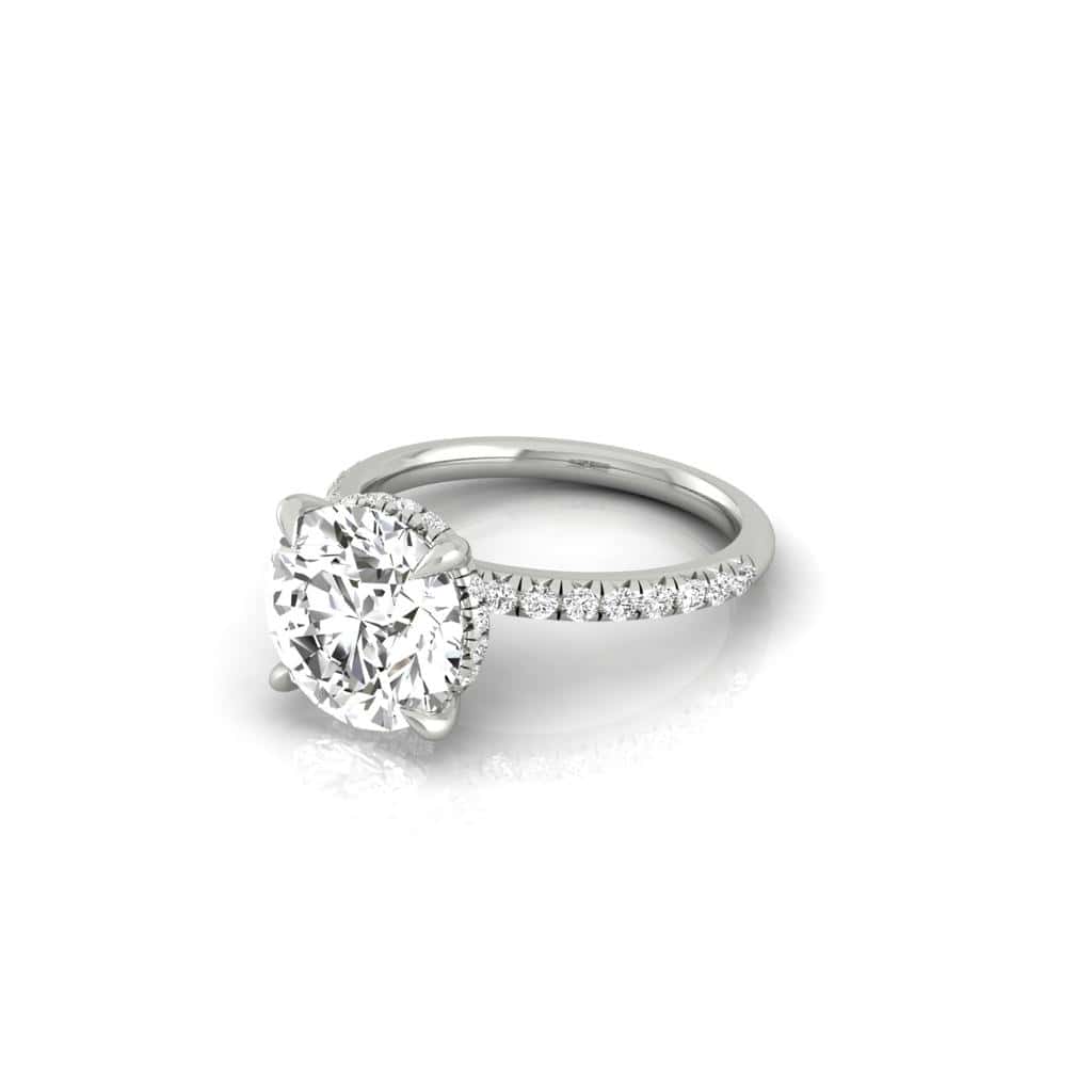 The Amélie + Full Halo Ring from Janet Heller Fine Jewelry features a single prong-set center diamond with a full halo of diamonds, set on a French Pavé band adorned with small diamonds. The ring can be worn alone or stacked with your wedding band.