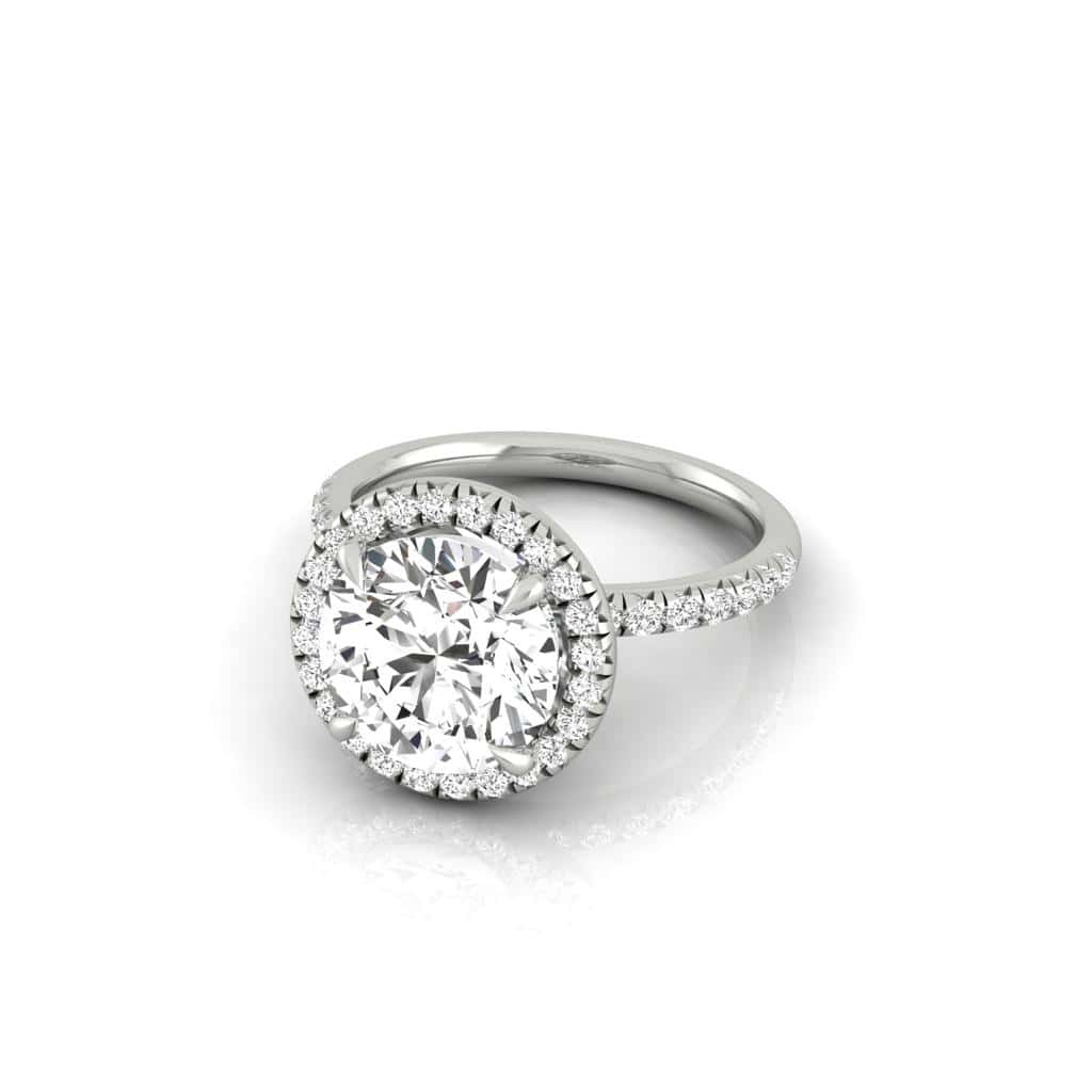 The Amélie + Full Halo silver engagement ring features a large center diamond surrounded by a dazzling halo. The French Pavé set band, adorned with extra diamonds, adds a sparkling touch as it gracefully rests on a reflective surface.