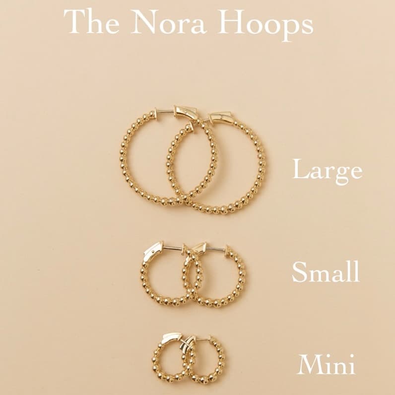 Three pairs of gold hoop earrings in varying sizes (labeled Large, Small, and Mini) are displayed vertically on a beige background beneath the title "The Nora Hoops." Featured here is the Small Nora Hoops style (SKU: EAR-1182-Y, $1,909.00). For custom jewelry requests or inquiries, please contact Janet Heller Fine Jewelry.