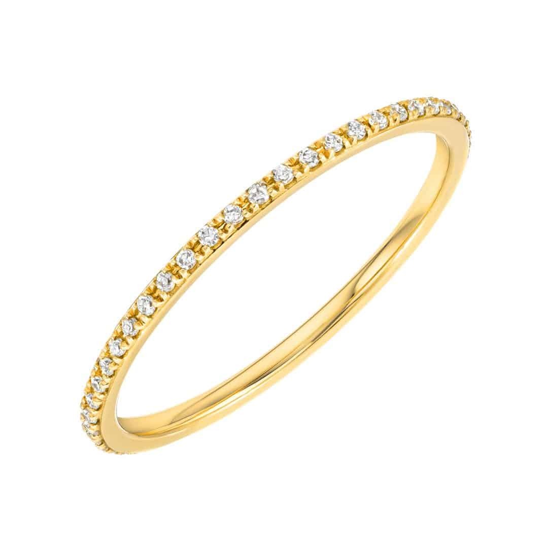 Introducing the Micro Pavé Eternity Ring, a thin gold band adorned with a row of delicate, sparkling white diamonds set along the top half. Elegantly presented on a white background, this fine jewelry piece by Janet Heller is perfect for preorders and ideal for those seeking timeless sophistication.