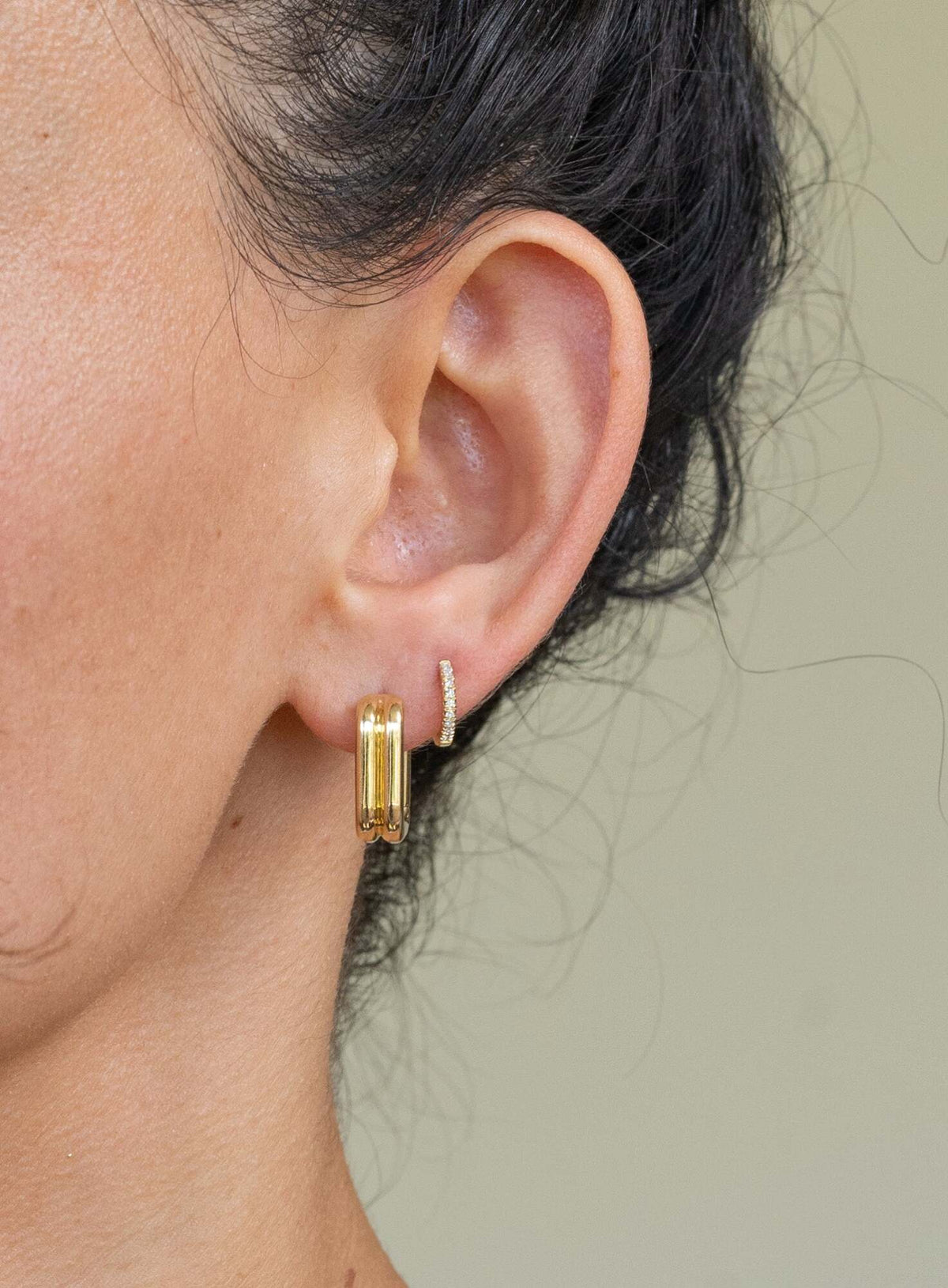 Close-up of a person’s ear adorned with two Mini Diamond Anika Huggies. Dark hair is pulled back, light brown skin glows—perfect inspiration for anyone seeking jewelry ideas or considering custom pieces.