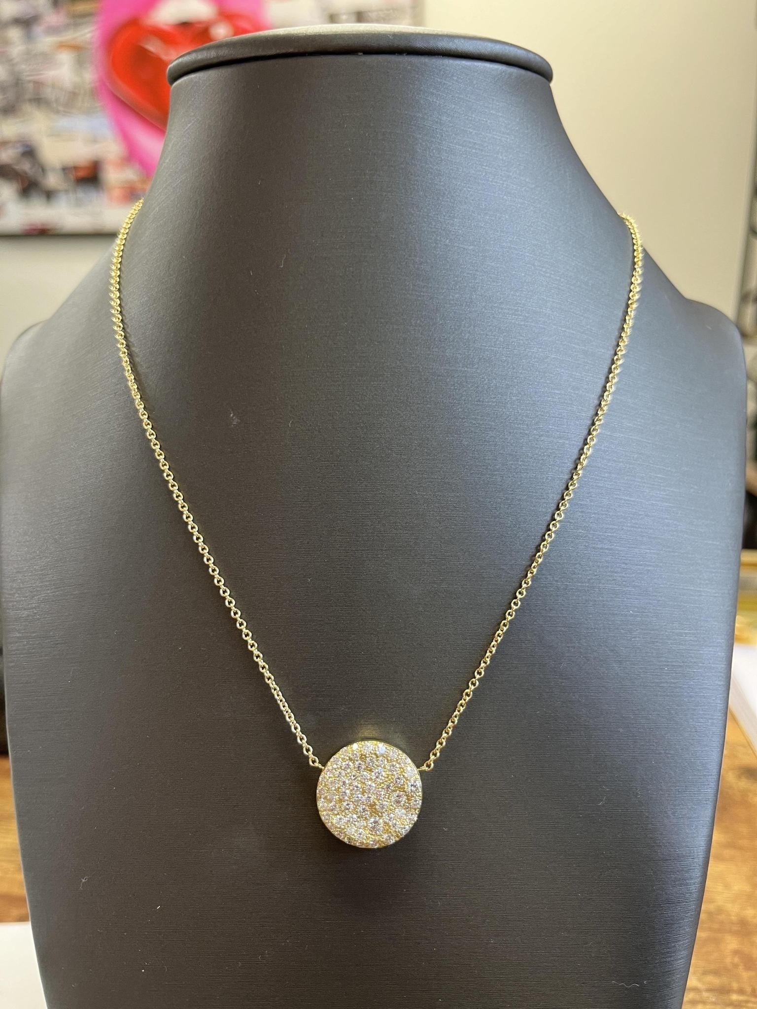 The Circle Diamond Mosaic Necklace from Janet Heller Fine Jewelry features a round, flat 18KT gold pendant adorned with diamonds, elegantly showcased on a black jewelry bust.